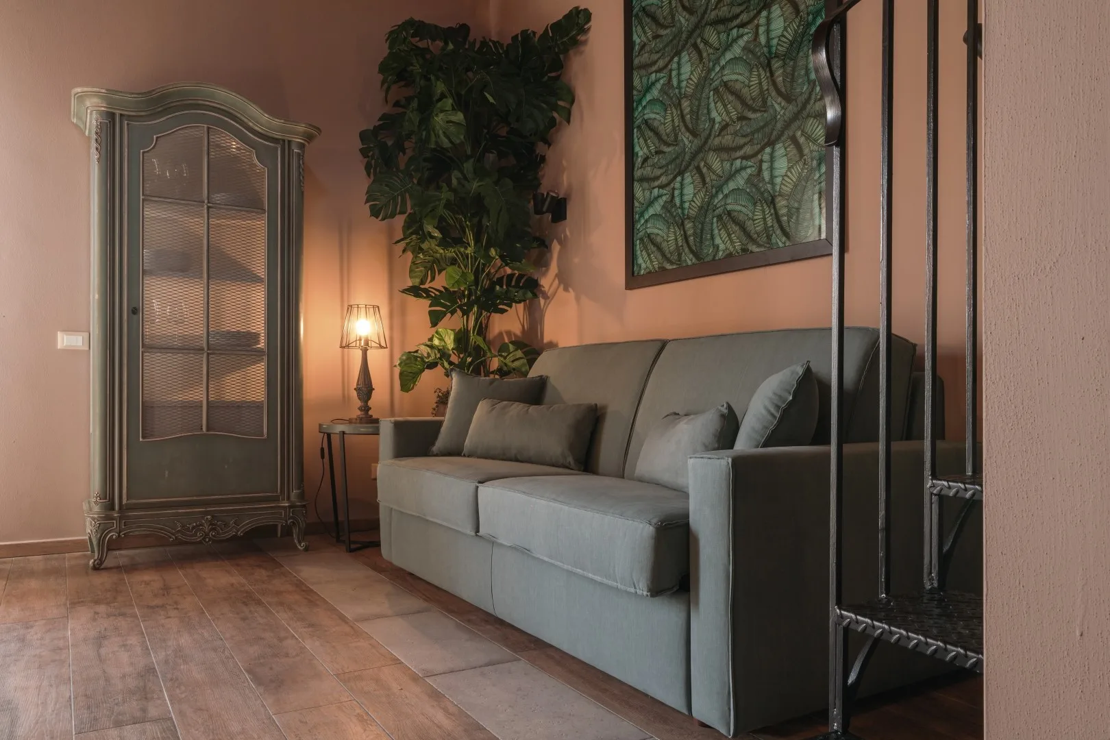 A living room with a gray sofa, tall cabinet, and leafy plant.