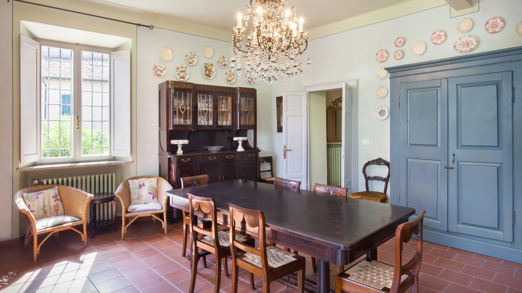 A dining room with a large table, wooden seating, and a chandelier.