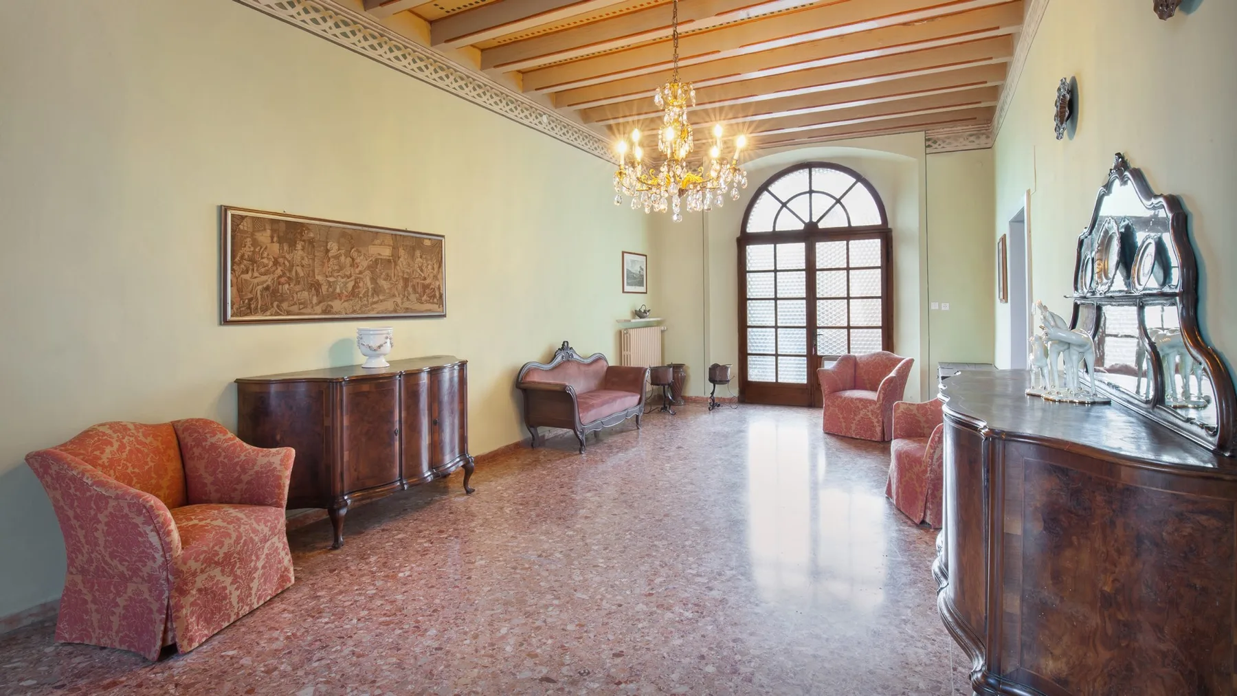 A spacious sitting room with upholstered seating and an arched window.