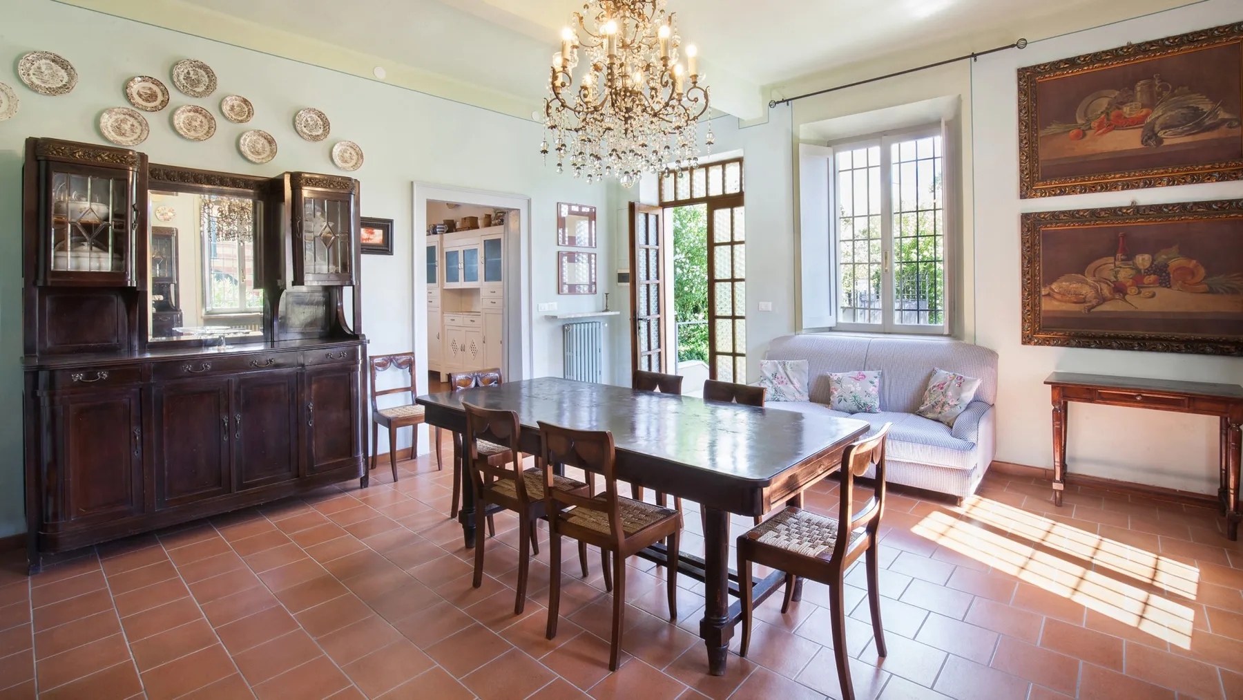 A bright dining room with a long wooden table, chairs, and a chandelier.