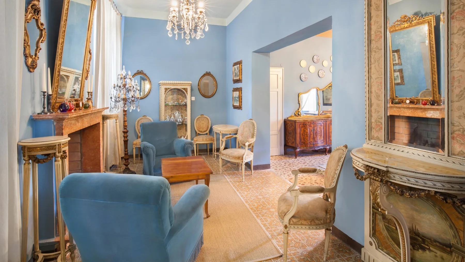 A blue sitting room with upholstered seating, a fireplace, and a chandelier.