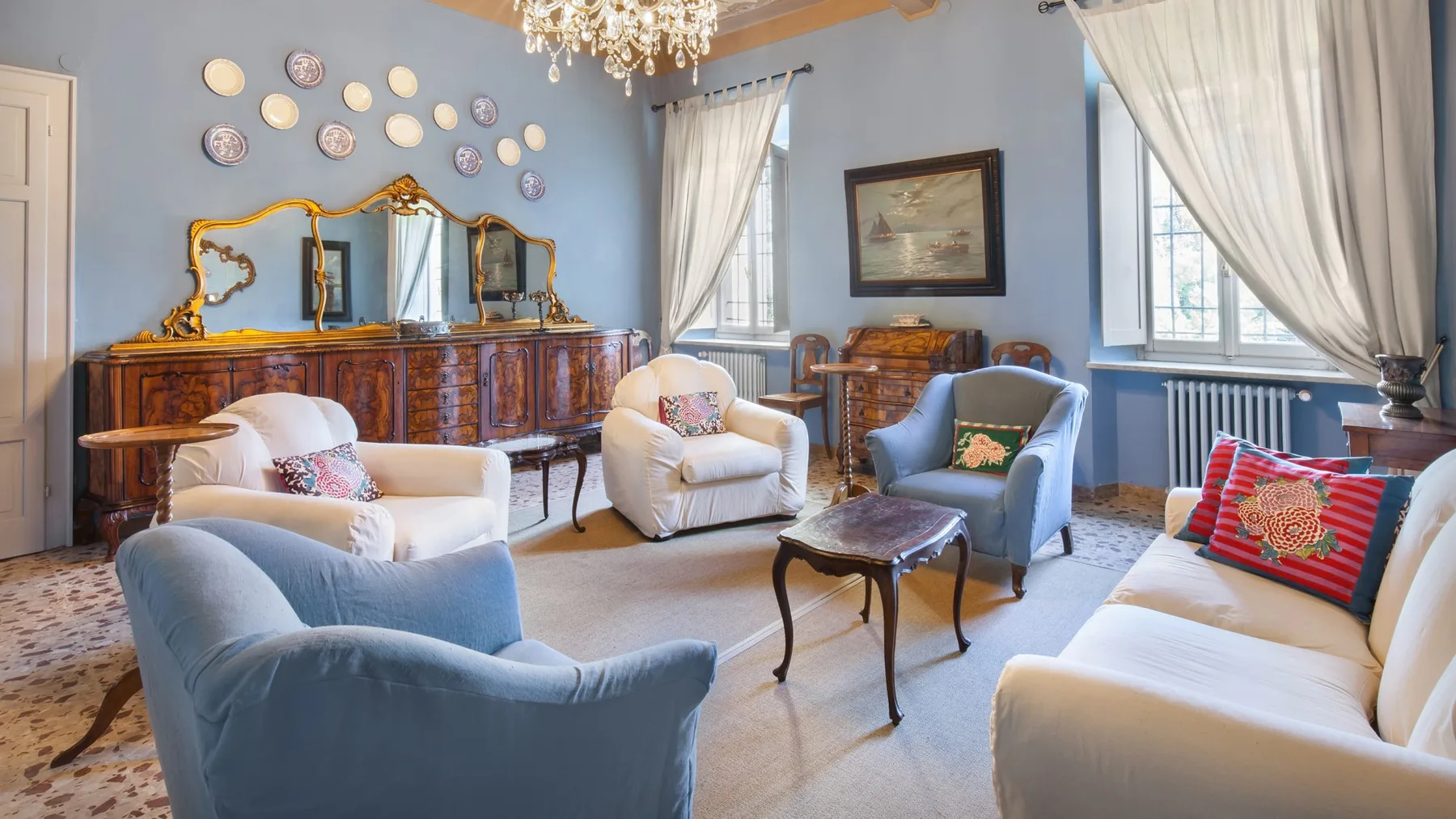 A living room with upholstered seating, a wooden coffee table, and tall curtained windows.
