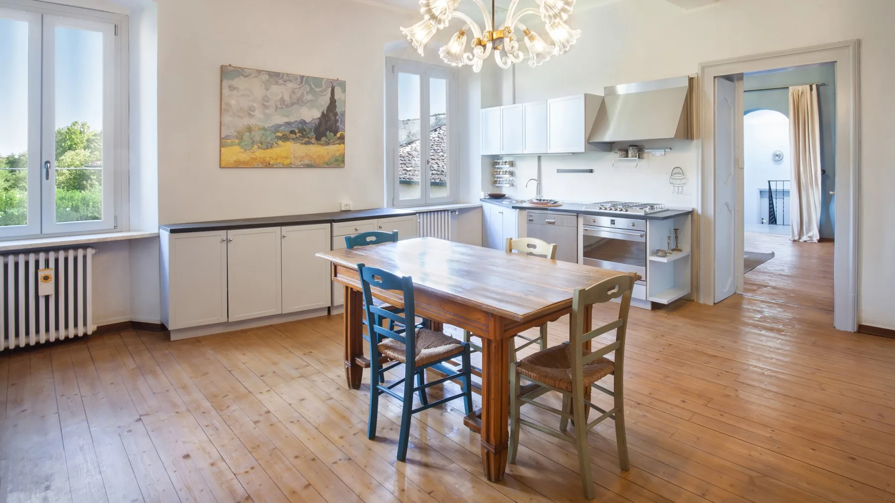 A dining area with a wooden table sits beside a bright kitchen.