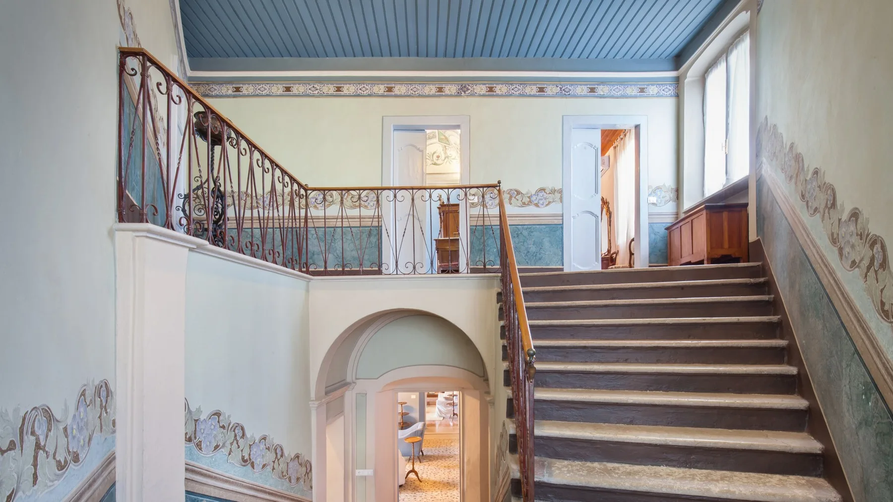 A stair hall with a broad staircase, ornate railing, and upper landing.