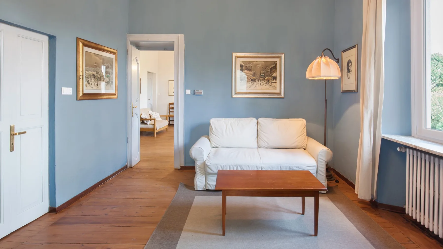 A living room with a white sofa, wooden coffee table, and framed wall art.