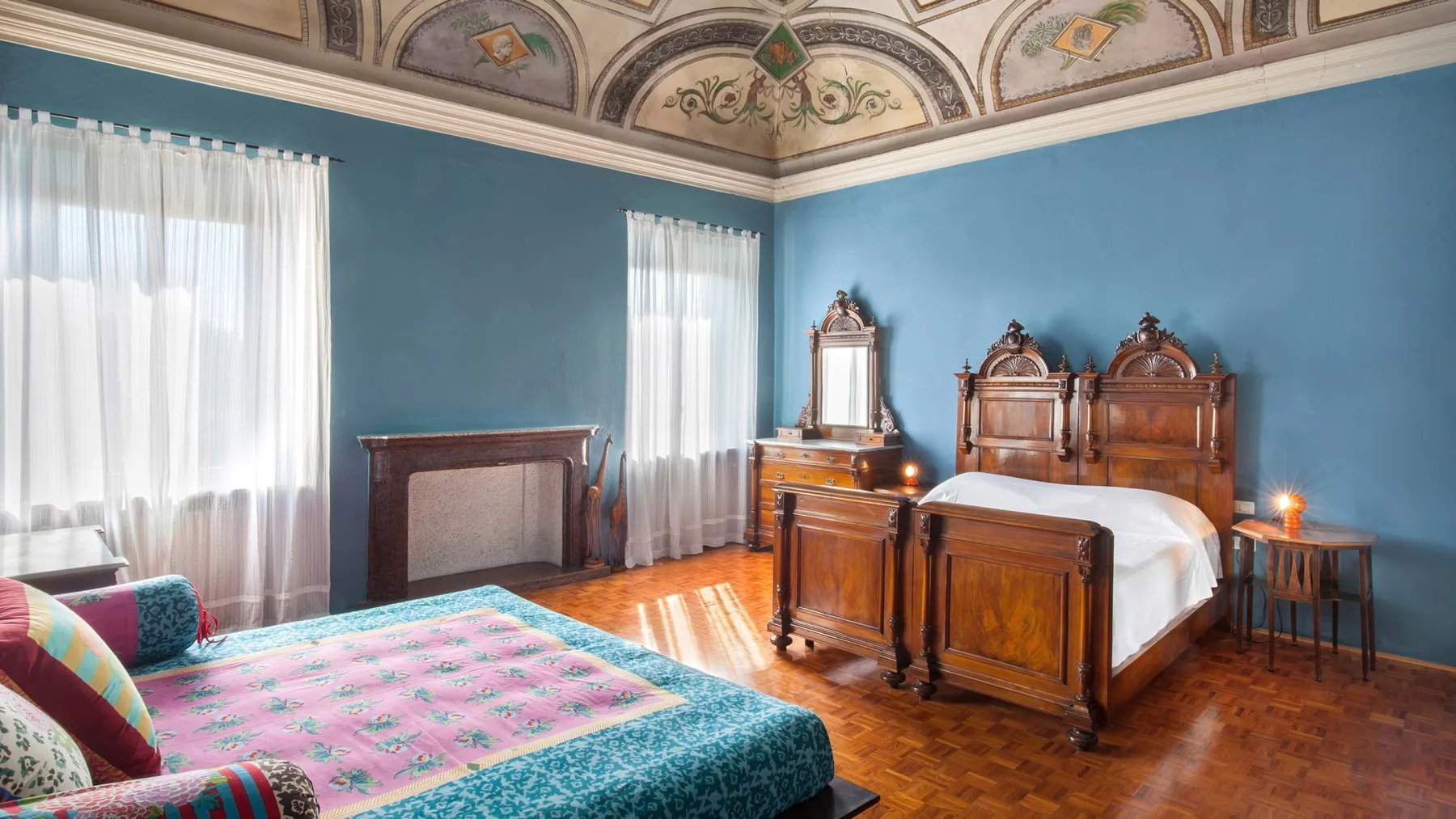 A bedroom with two wooden beds, blue walls, and a colorful patterned rug.