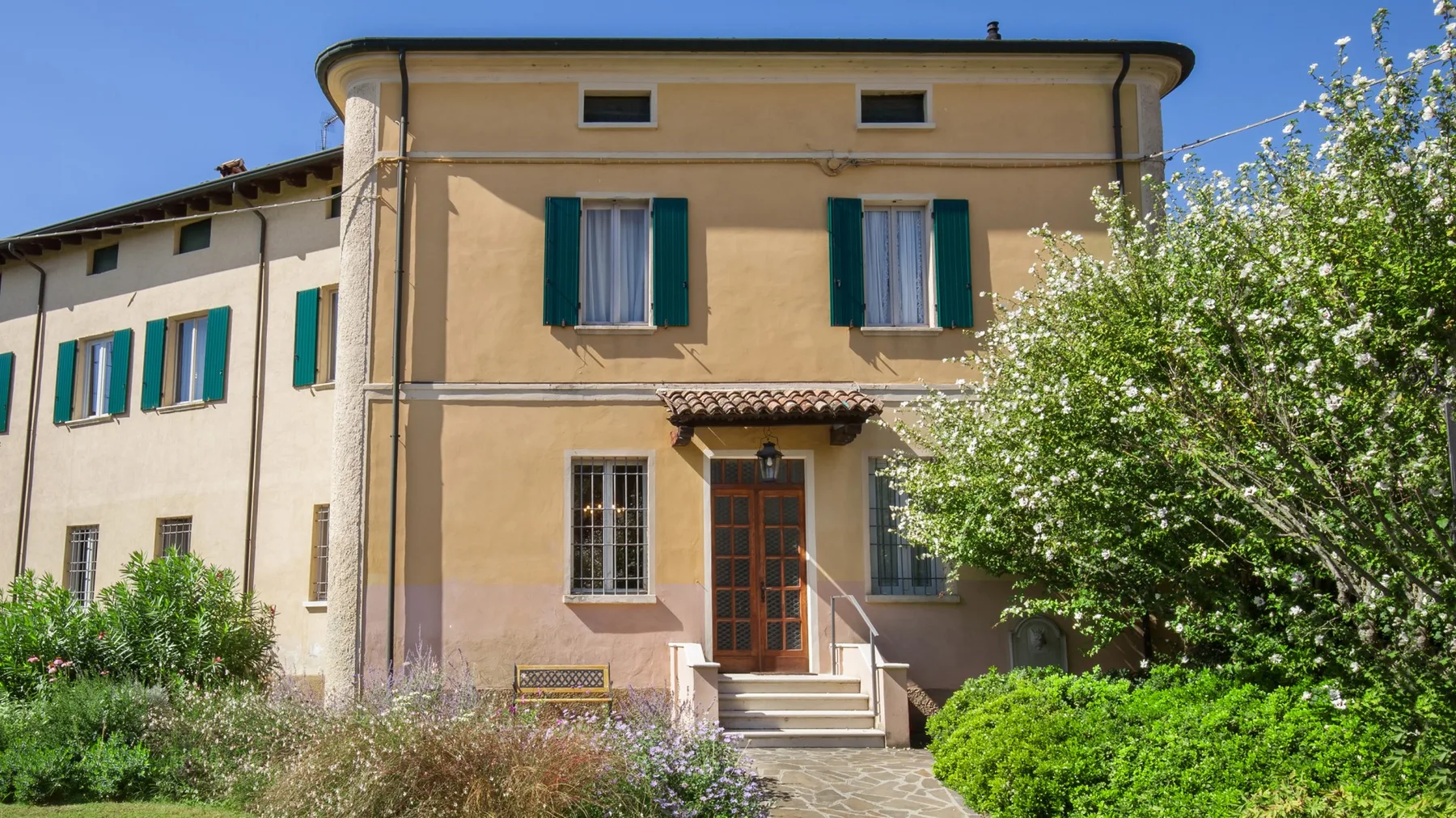 A two-story house with green shutters and a central entrance.