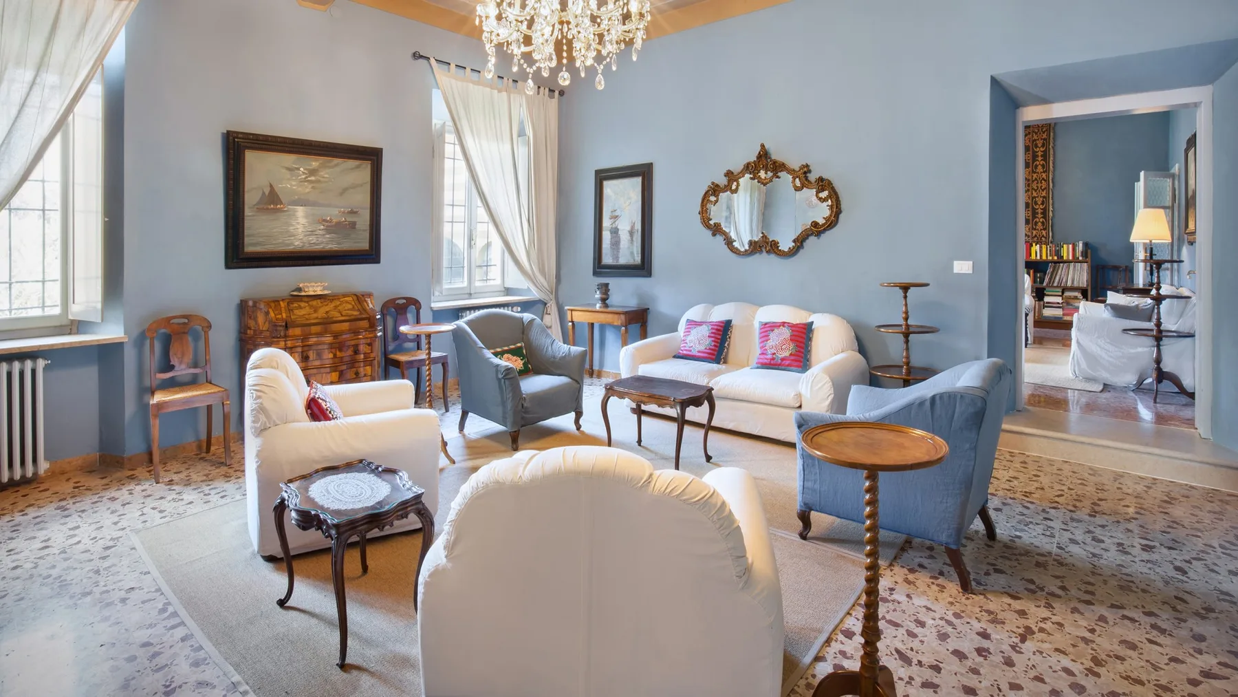 A bright living room with upholstered seating, small tables, and a chandelier.