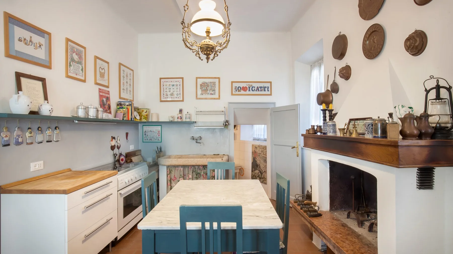 A bright kitchen with a long dining table, blue chairs, and a fireplace.