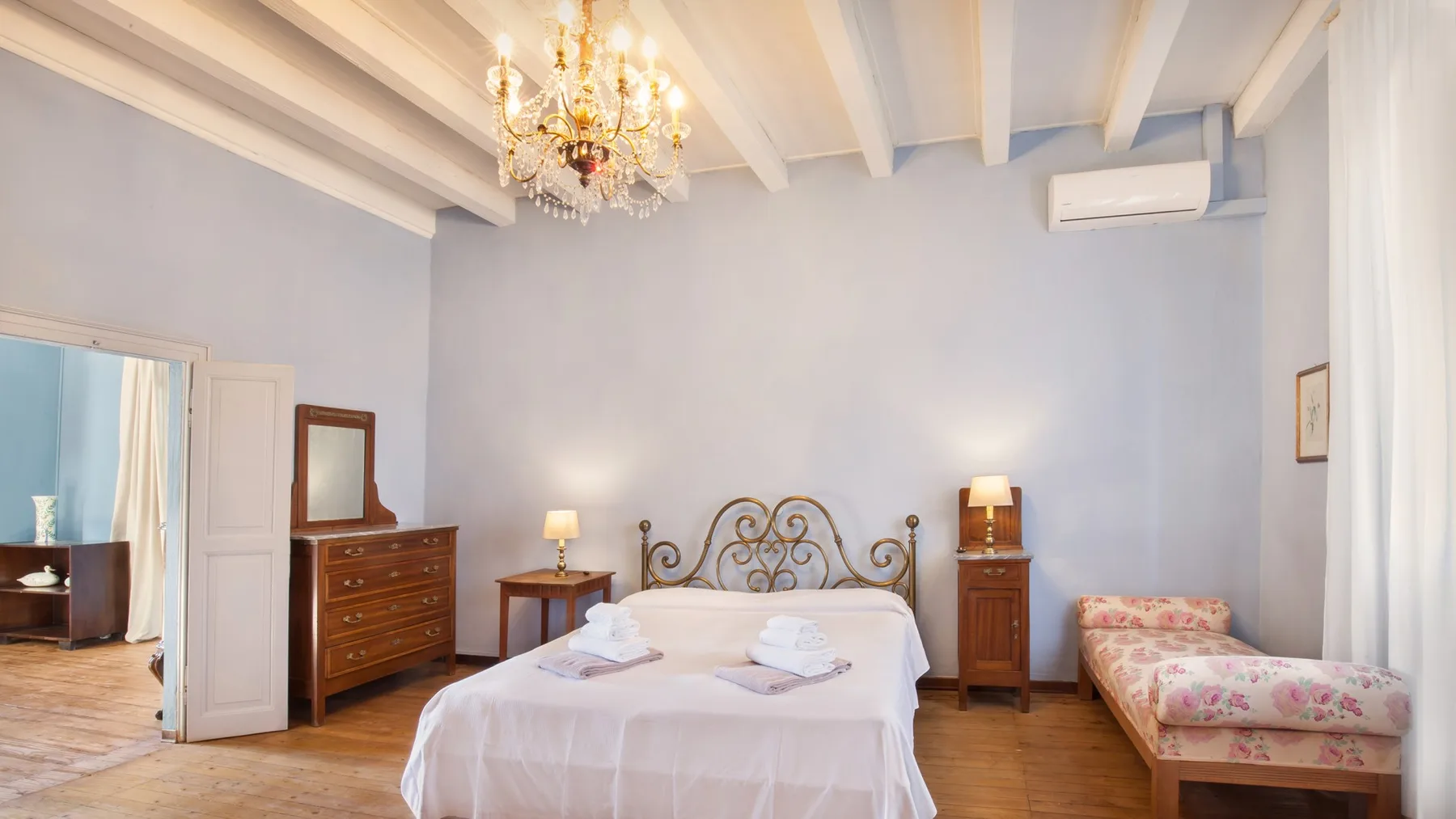 A bedroom with a bed, wooden furniture, and a floral upholstered seat.