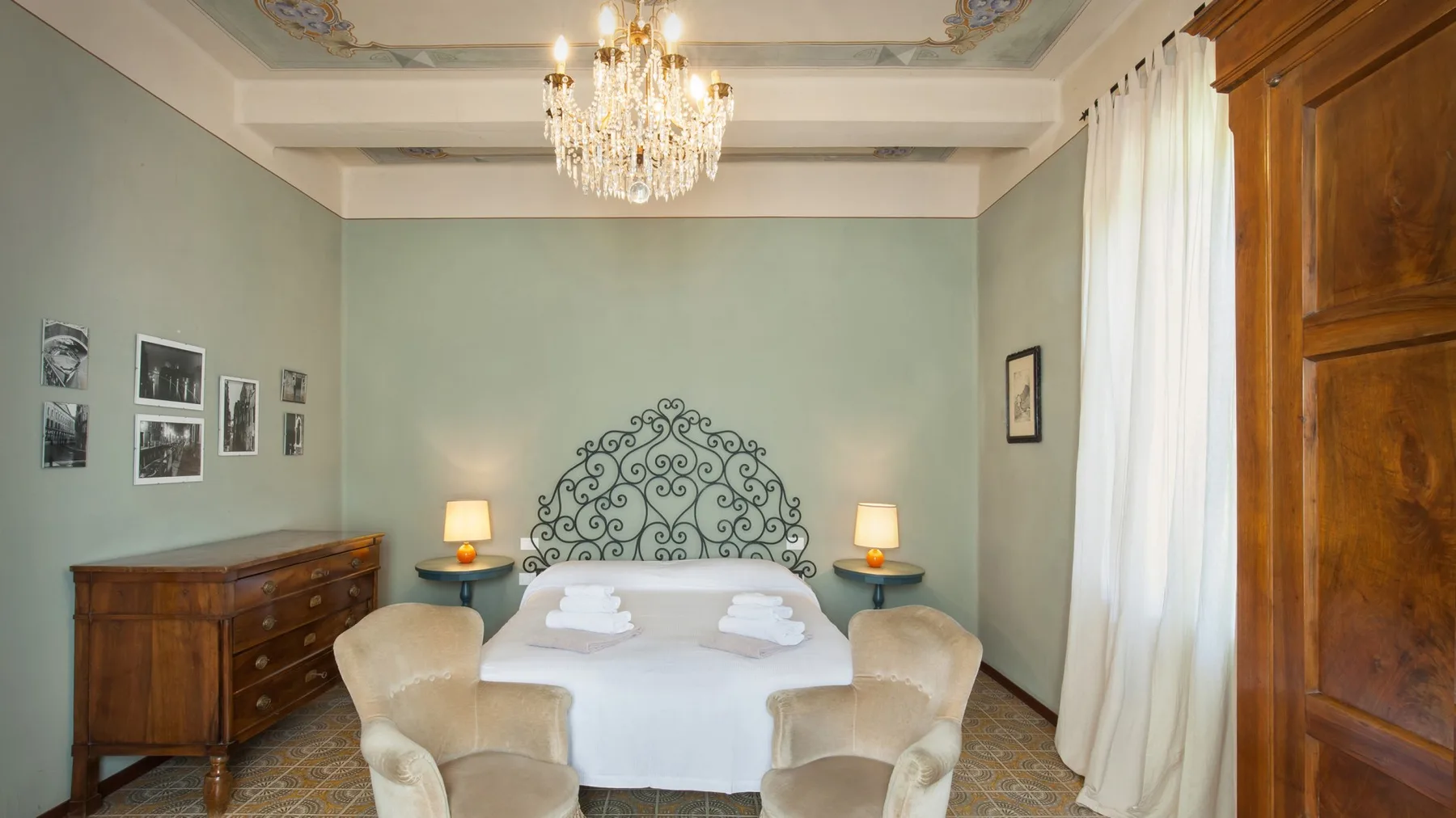 A bedroom with a bed, two armchairs, and a wooden chest of drawers.