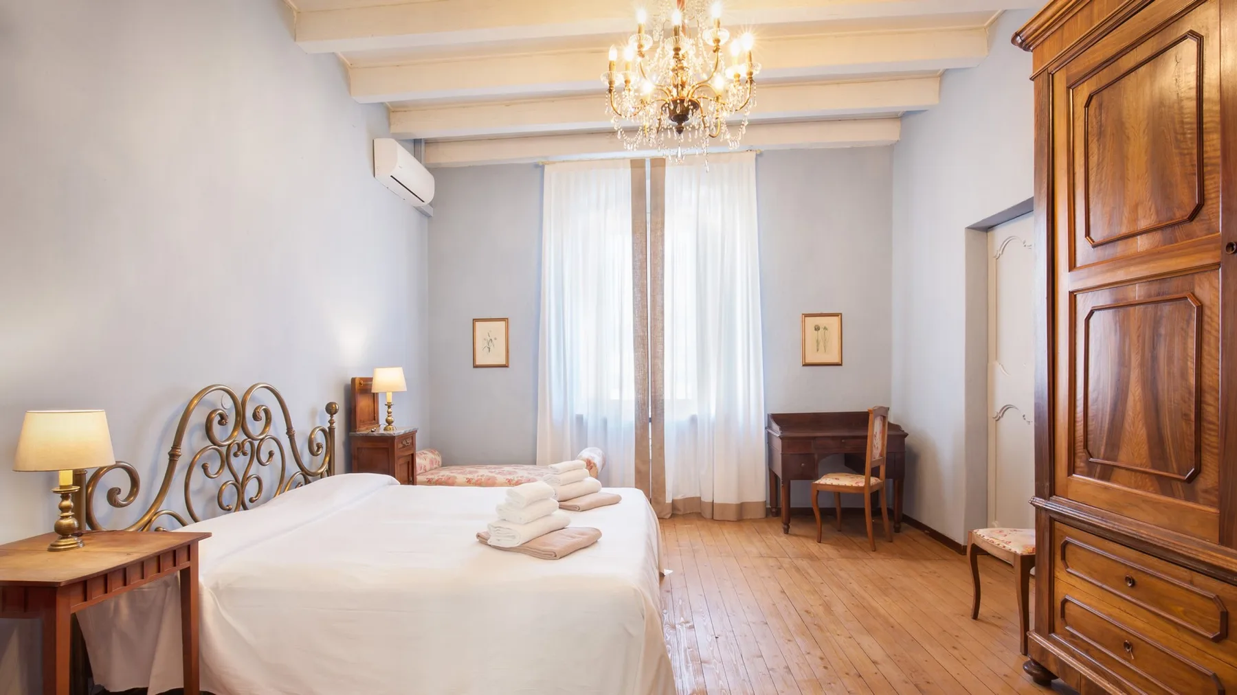 A bedroom with a bed, wooden flooring, and a tall wooden wardrobe.