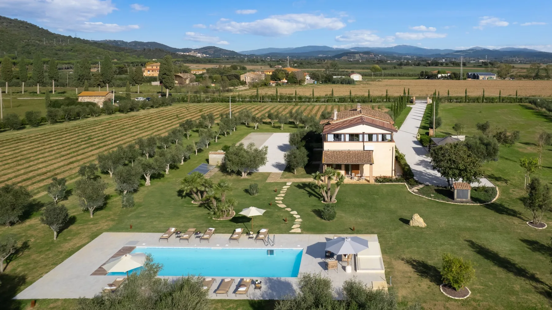 A countryside property with a swimming pool, landscaped lawn, and fields beyond.