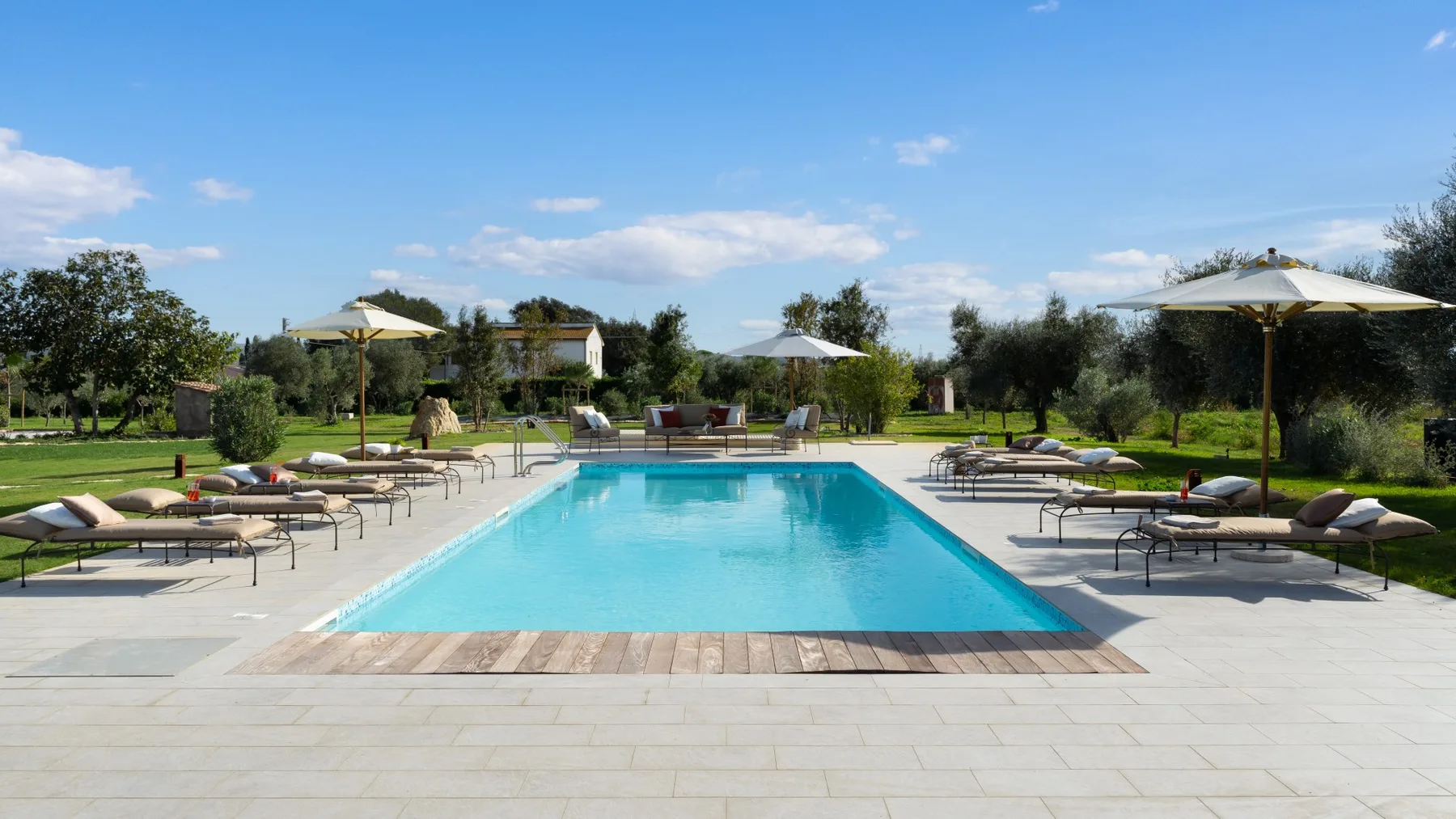 An outdoor swimming pool is surrounded by lounge seating and umbrellas.