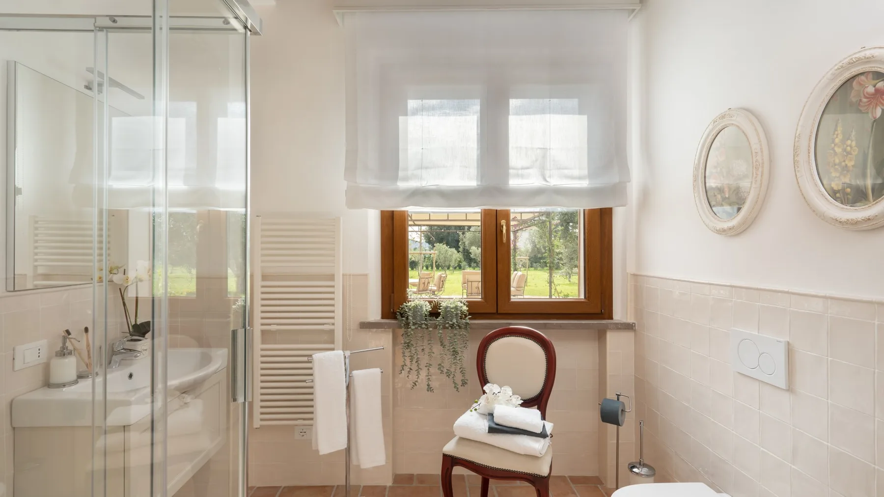 A bright bathroom with a glass shower, sink, and window overlooking greenery.