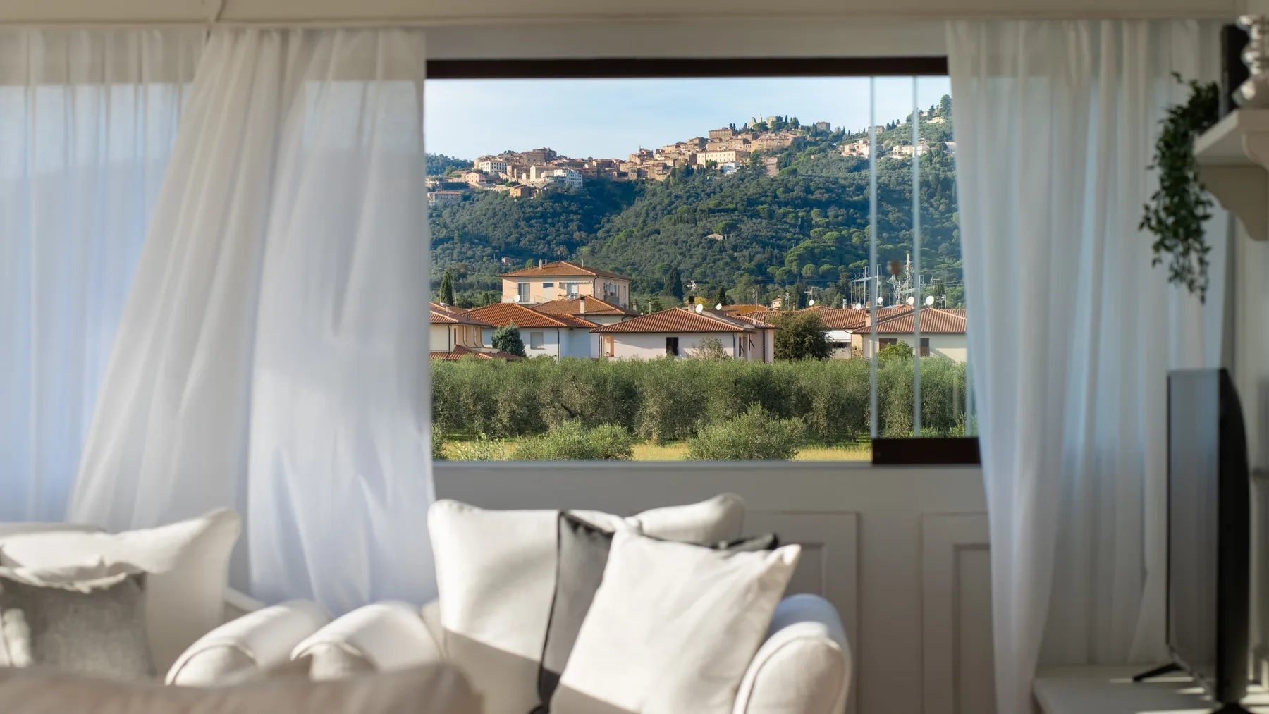 A bright living room has a sofa by a large window overlooking a green hillside.