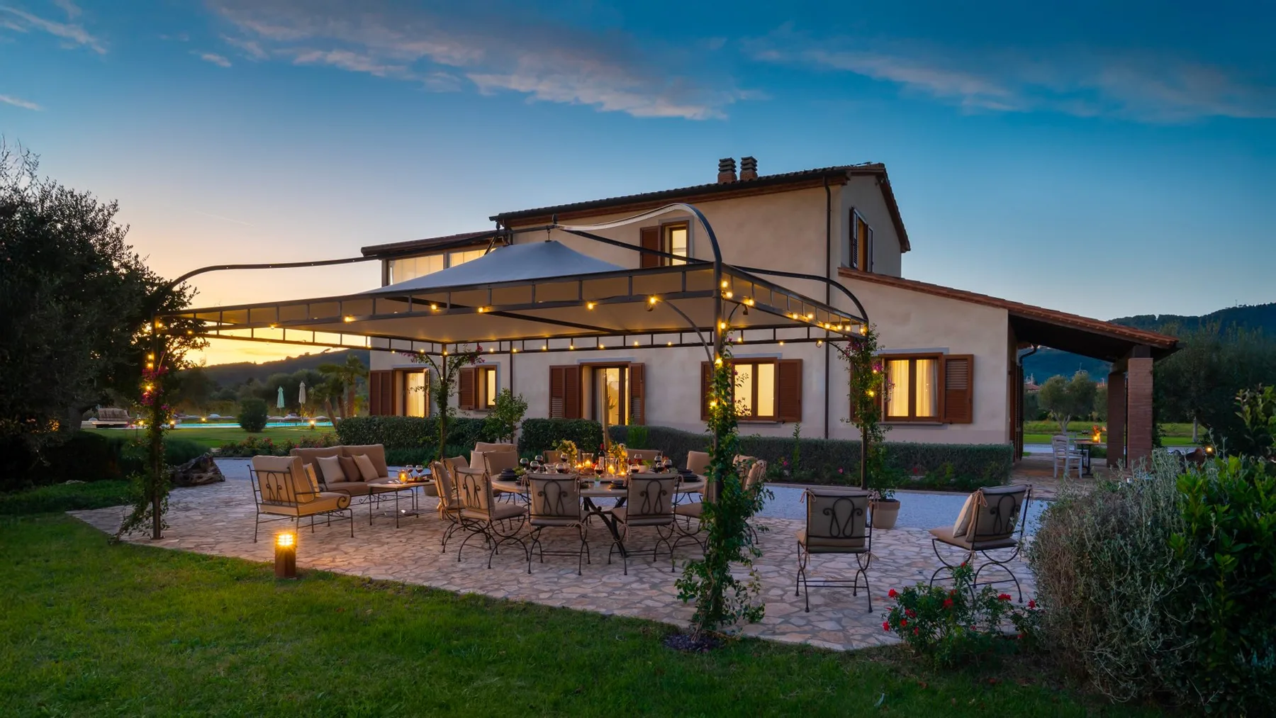 A house with a broad outdoor patio, seating, and a canopy at dusk.