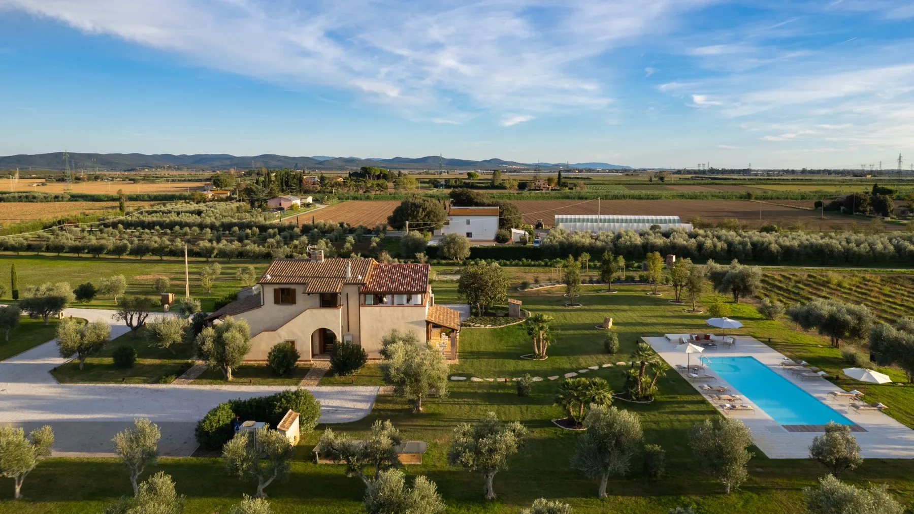 A countryside property with a swimming pool, gardens, and fields beyond.