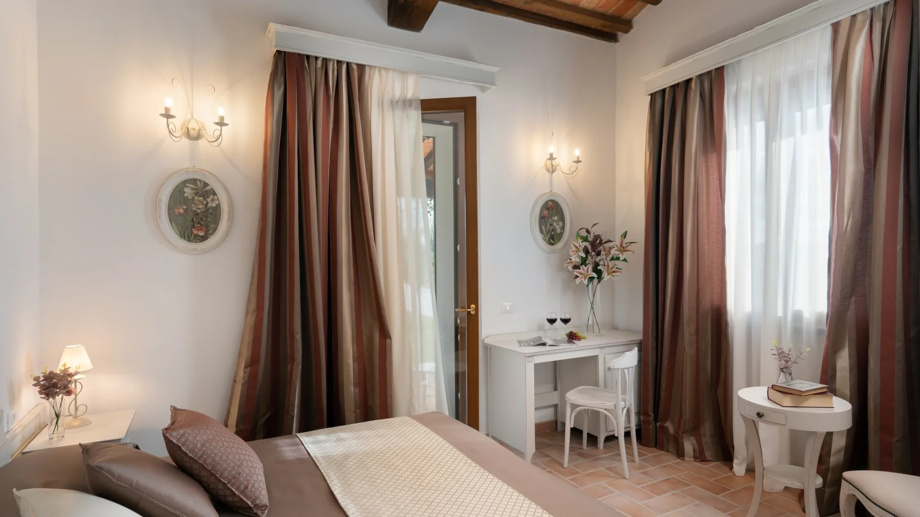 A bedroom with a bed, a small desk, and tall curtained windows.