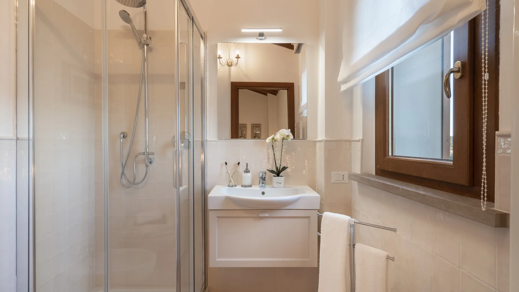 A bright bathroom with a glass shower, sink, and window.