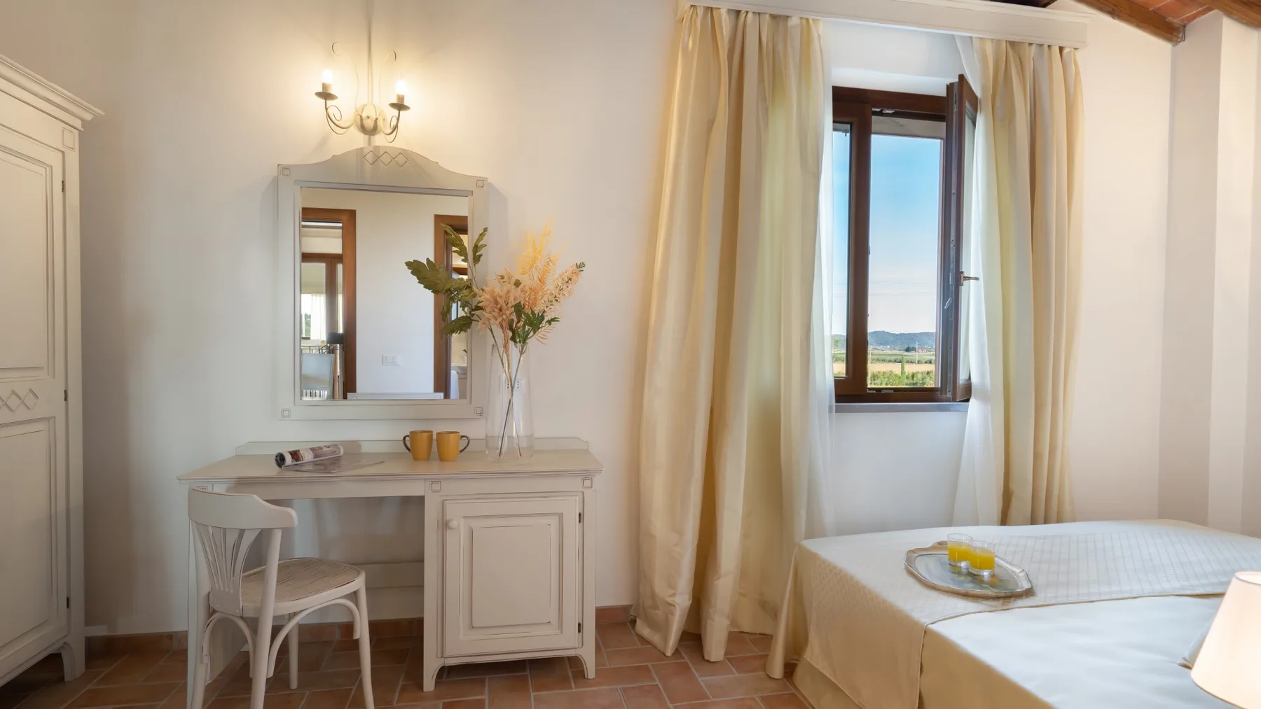 A bedroom with a bed beside a dressing table and a window with curtains.