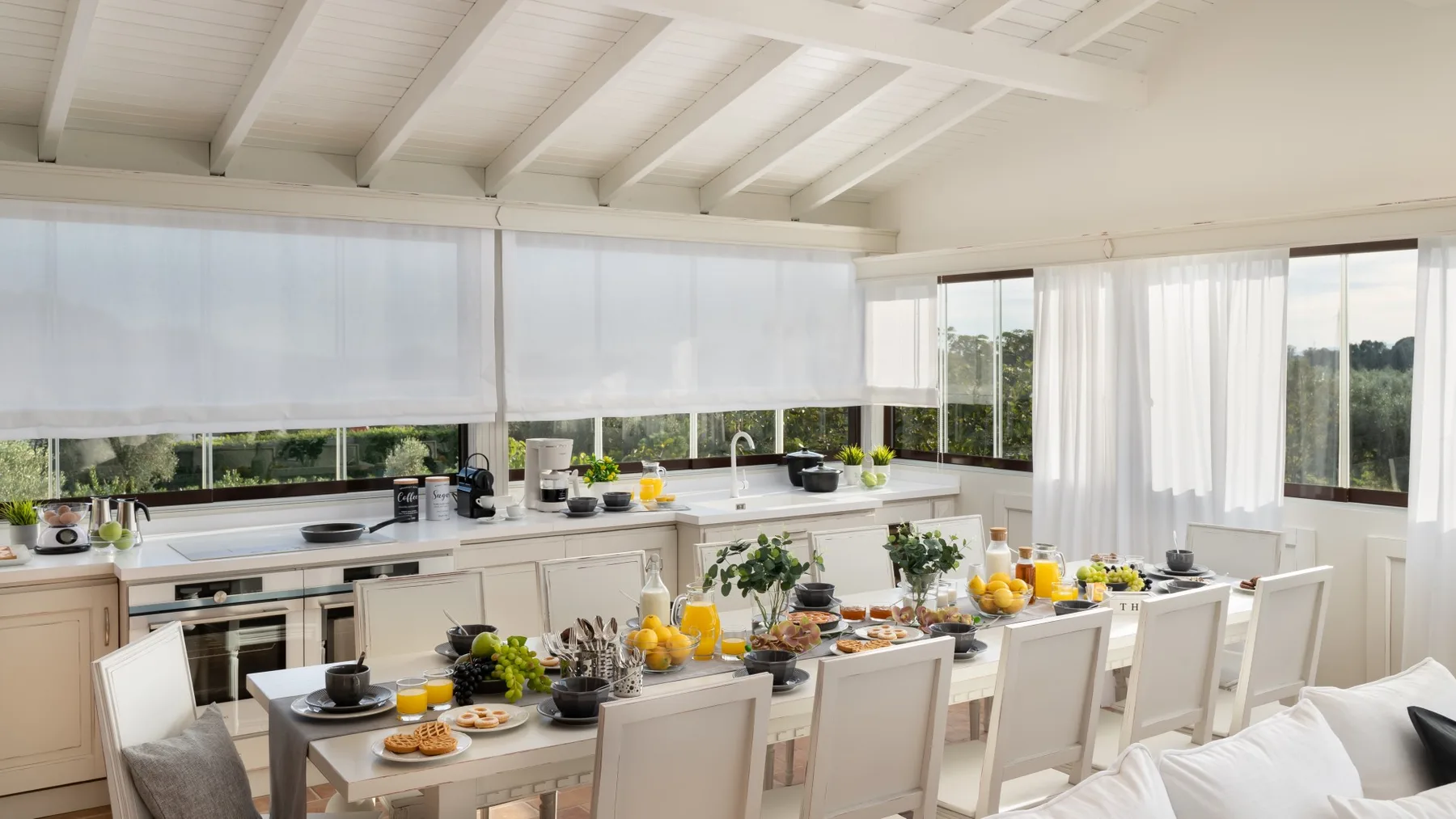A bright kitchen and dining area with a long table set beside large windows.