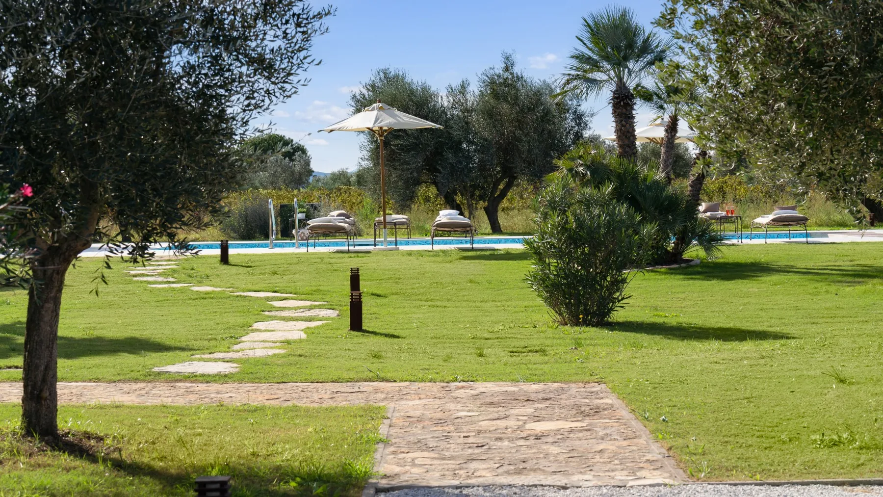 A landscaped garden path leads across a lawn toward a swimming pool.