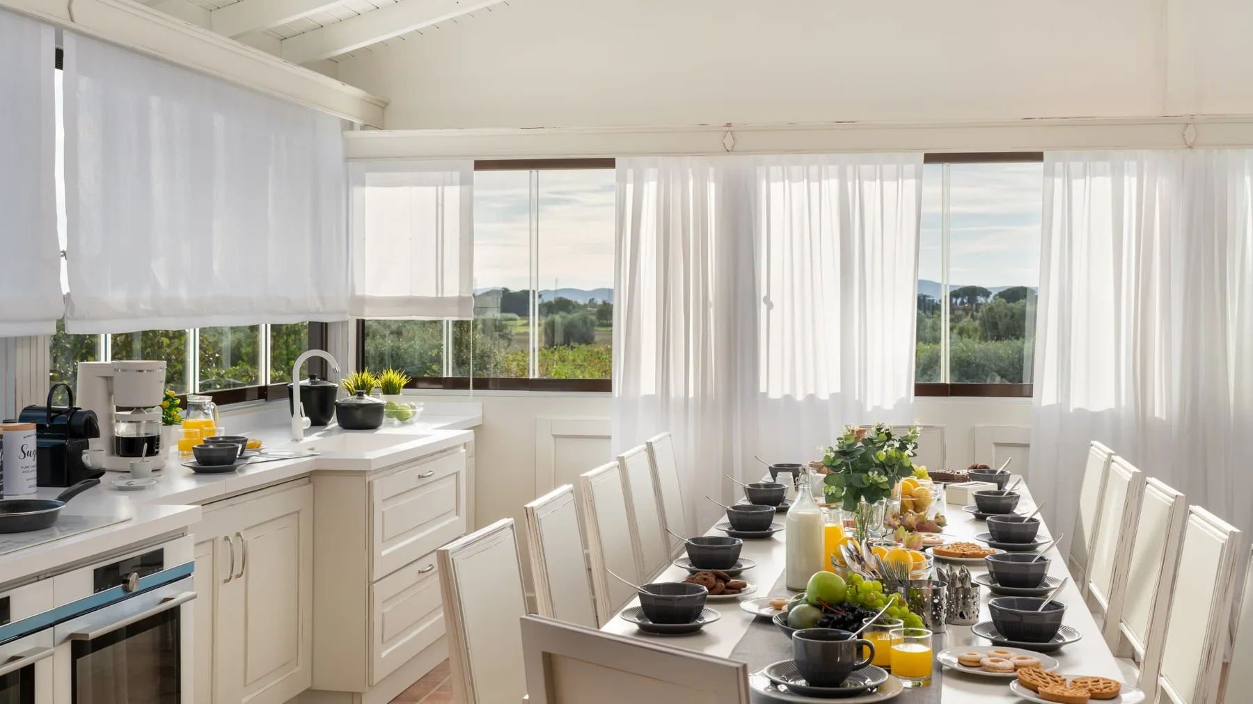A bright dining area with a long table set beside large windows.