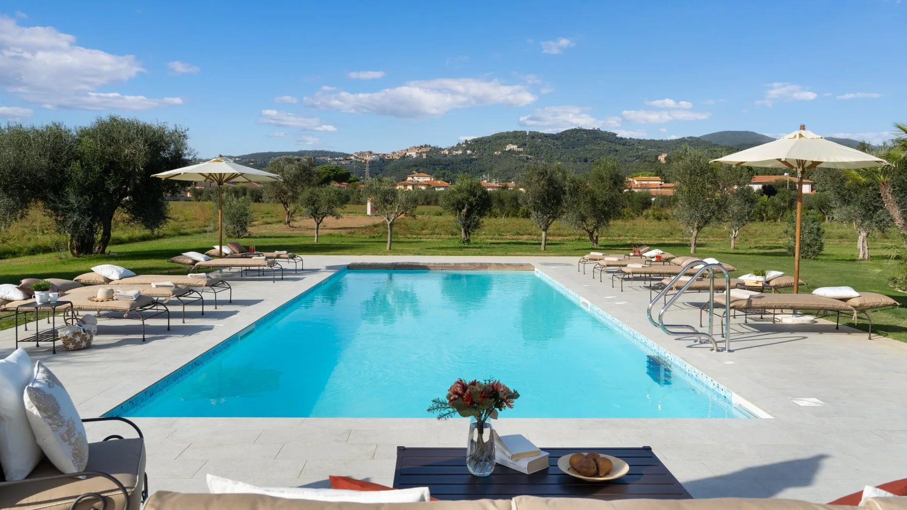 An outdoor swimming pool is surrounded by loungers and umbrellas.
