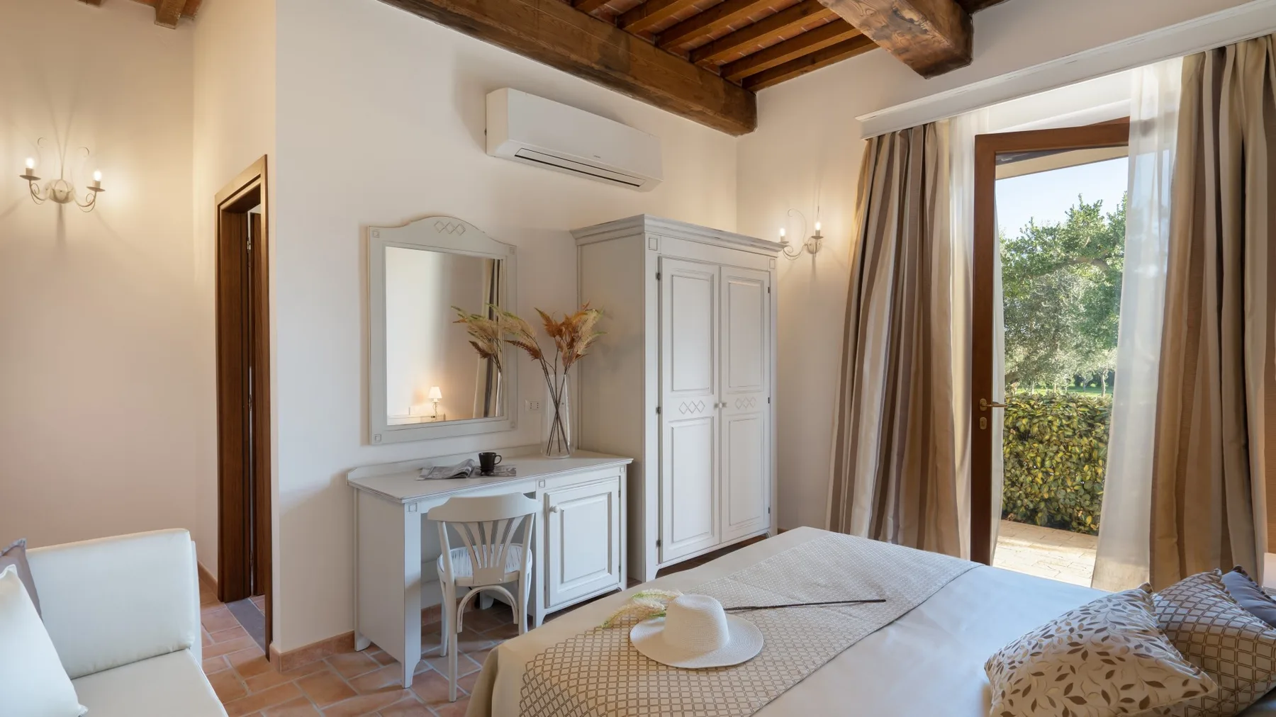 A bedroom with a bed, a white dressing table, and a glass door opening to greenery.