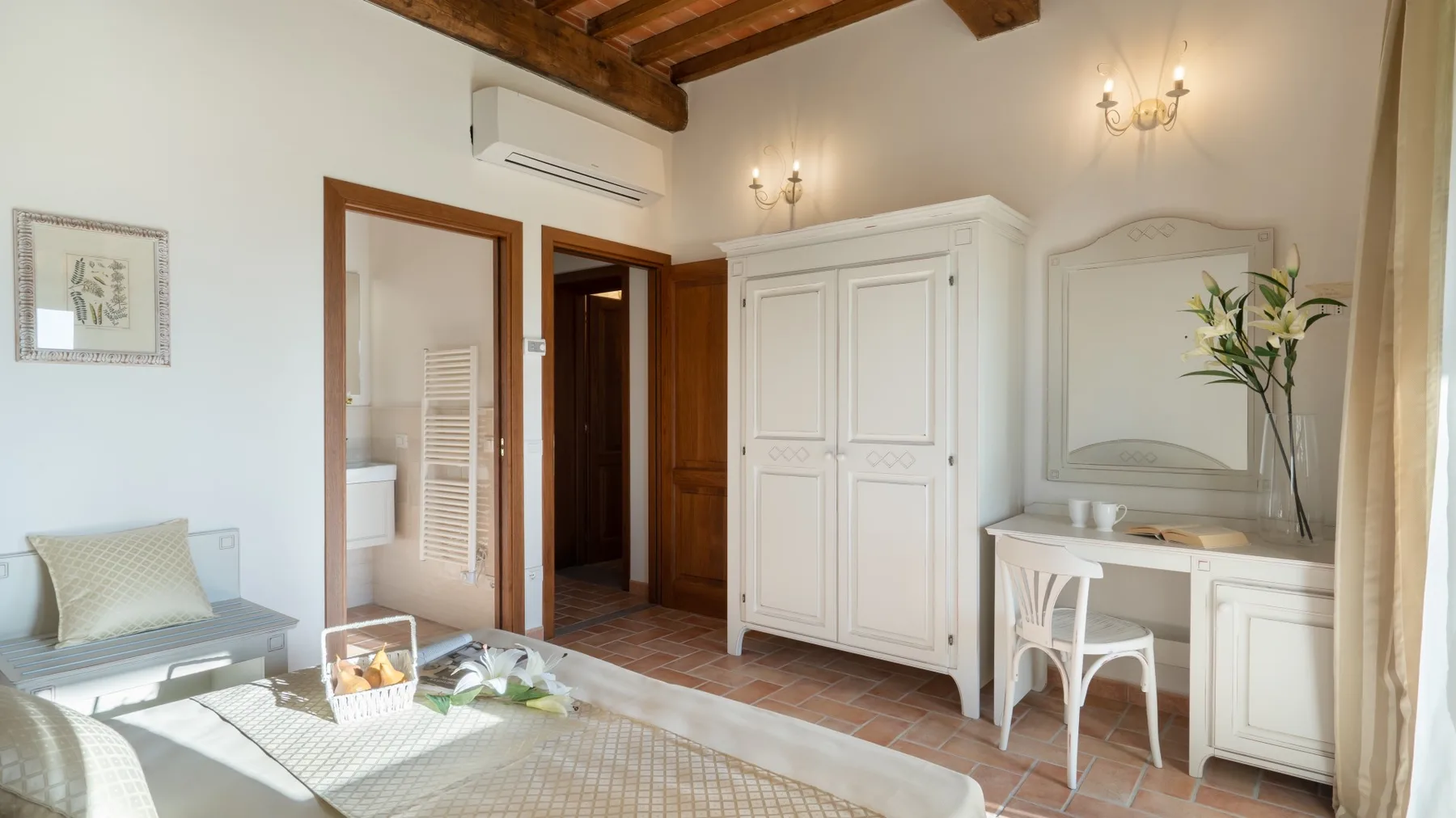 A bright bedroom with a white wardrobe, vanity, and wooden ceiling beams.