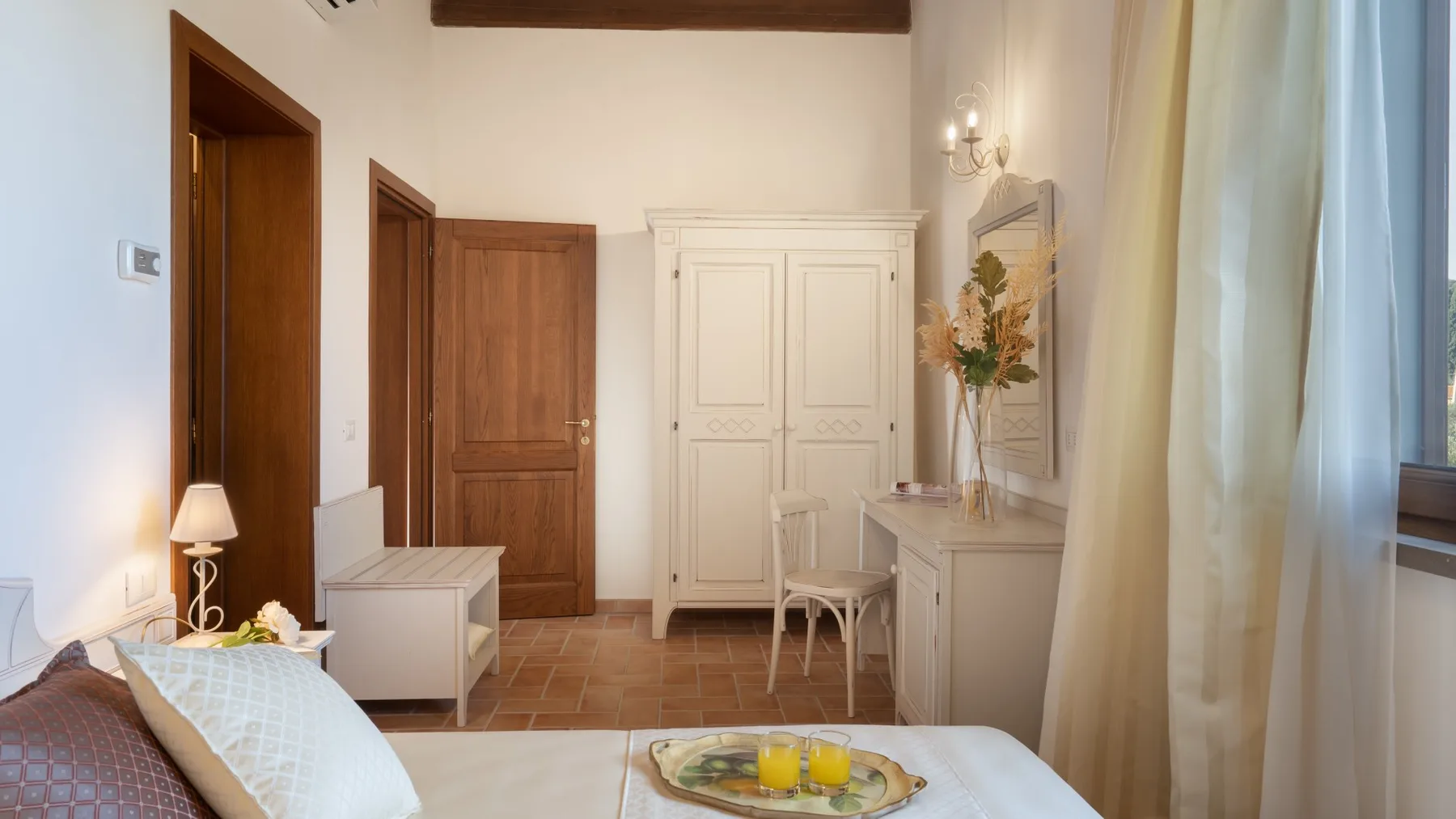 A bedroom with a bed, a white wardrobe, and a small writing desk.
