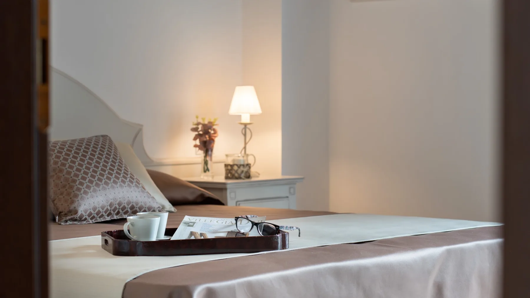 A bedroom with a neatly made bed and a bedside lamp.