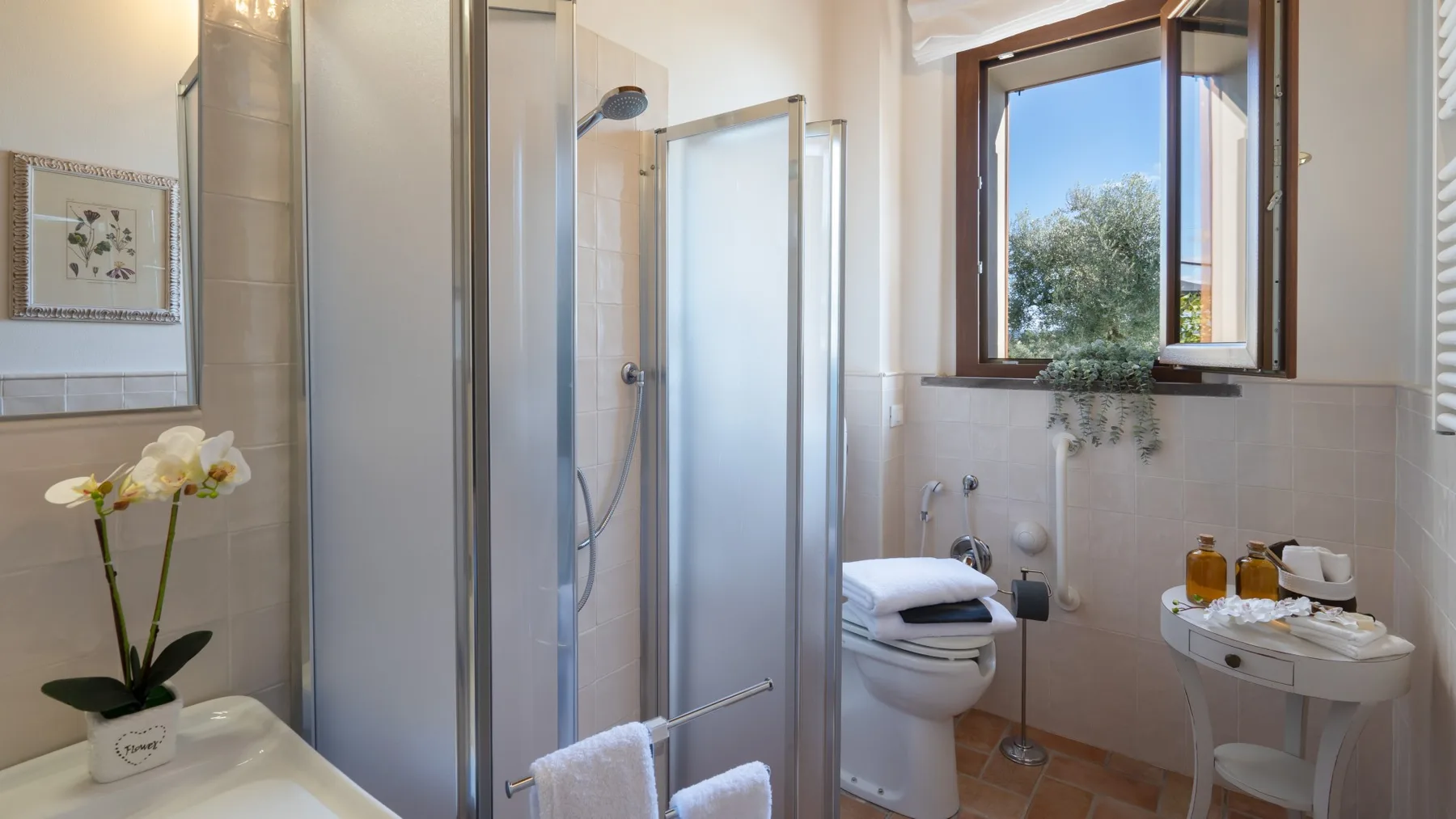 A bathroom with a glass shower and a window overlooking trees.