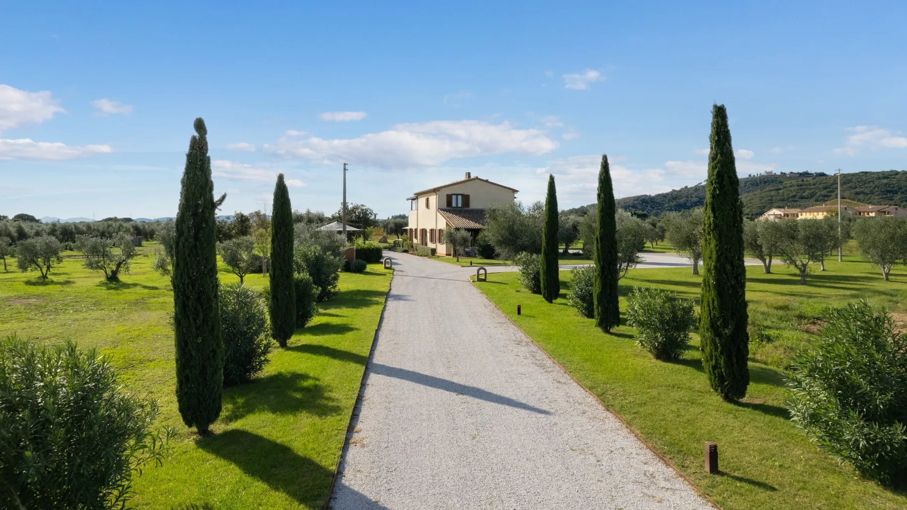 A paved driveway runs through landscaped grounds toward a house.