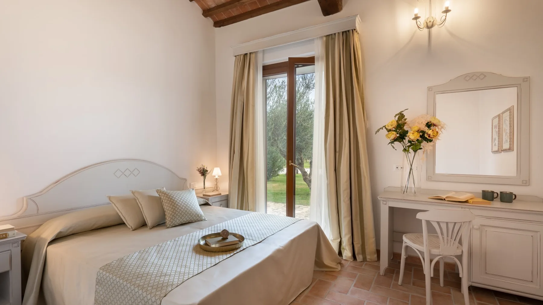 A bedroom with a double bed, a writing desk, and glass doors opening to a garden.
