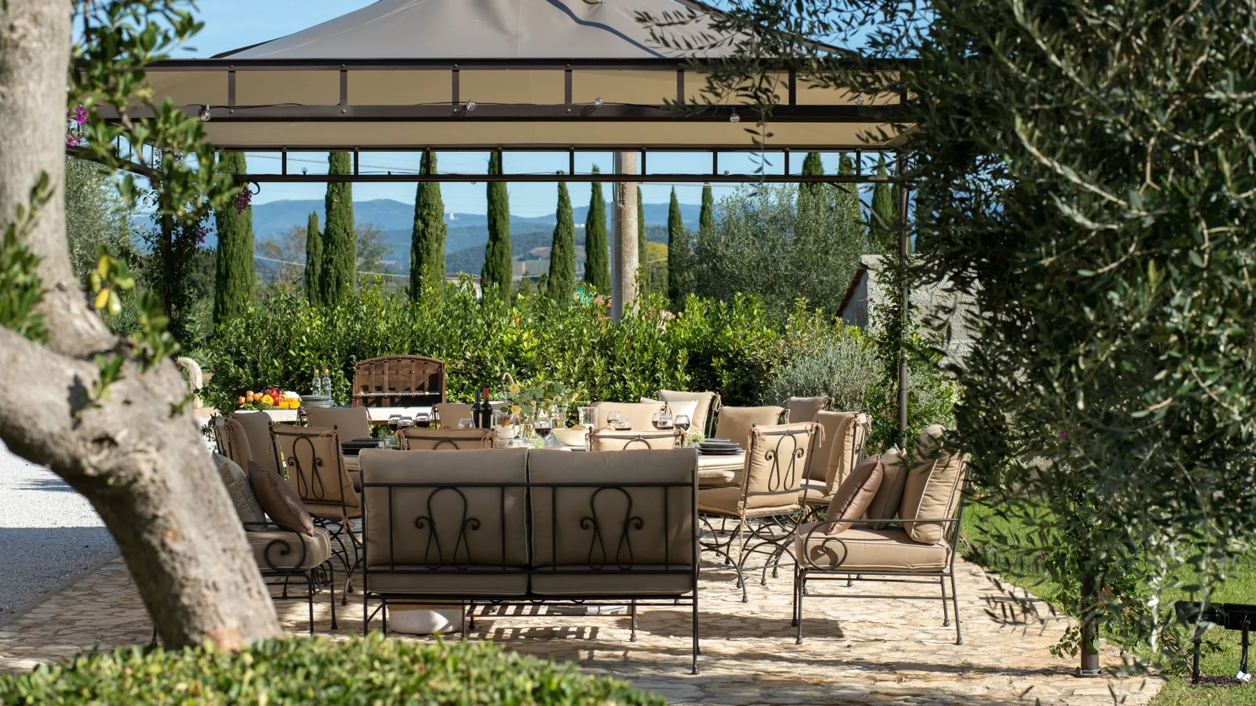 An outdoor dining area with a long table and cushioned seating beneath a canopy.