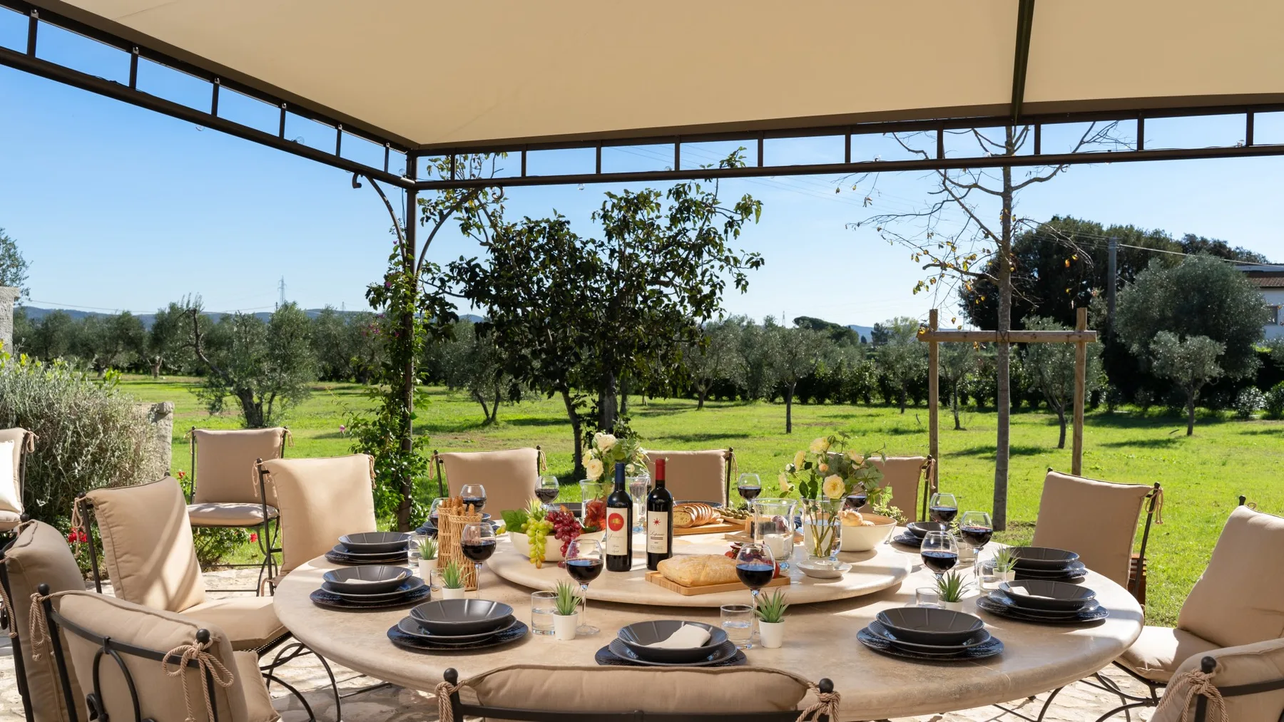 A covered outdoor dining area with a set table overlooking a green landscape.