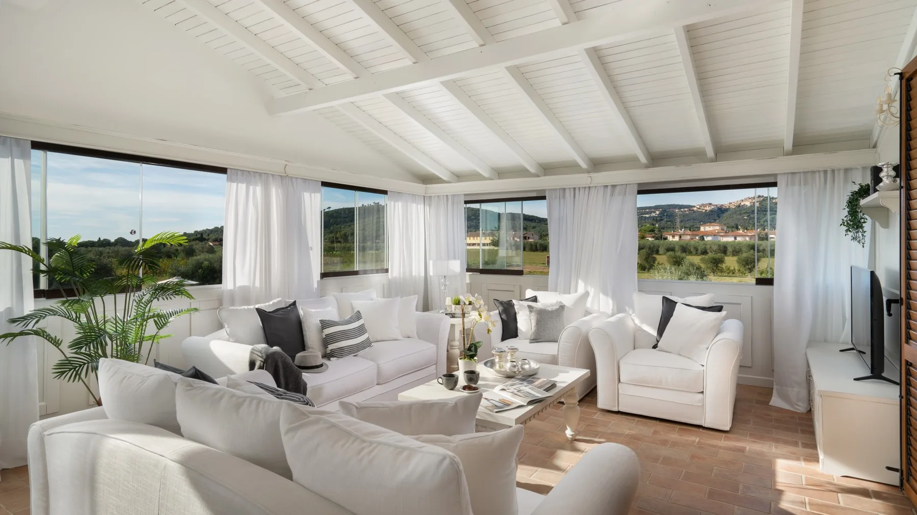 A bright living room with white seating and wide windows overlooking greenery.