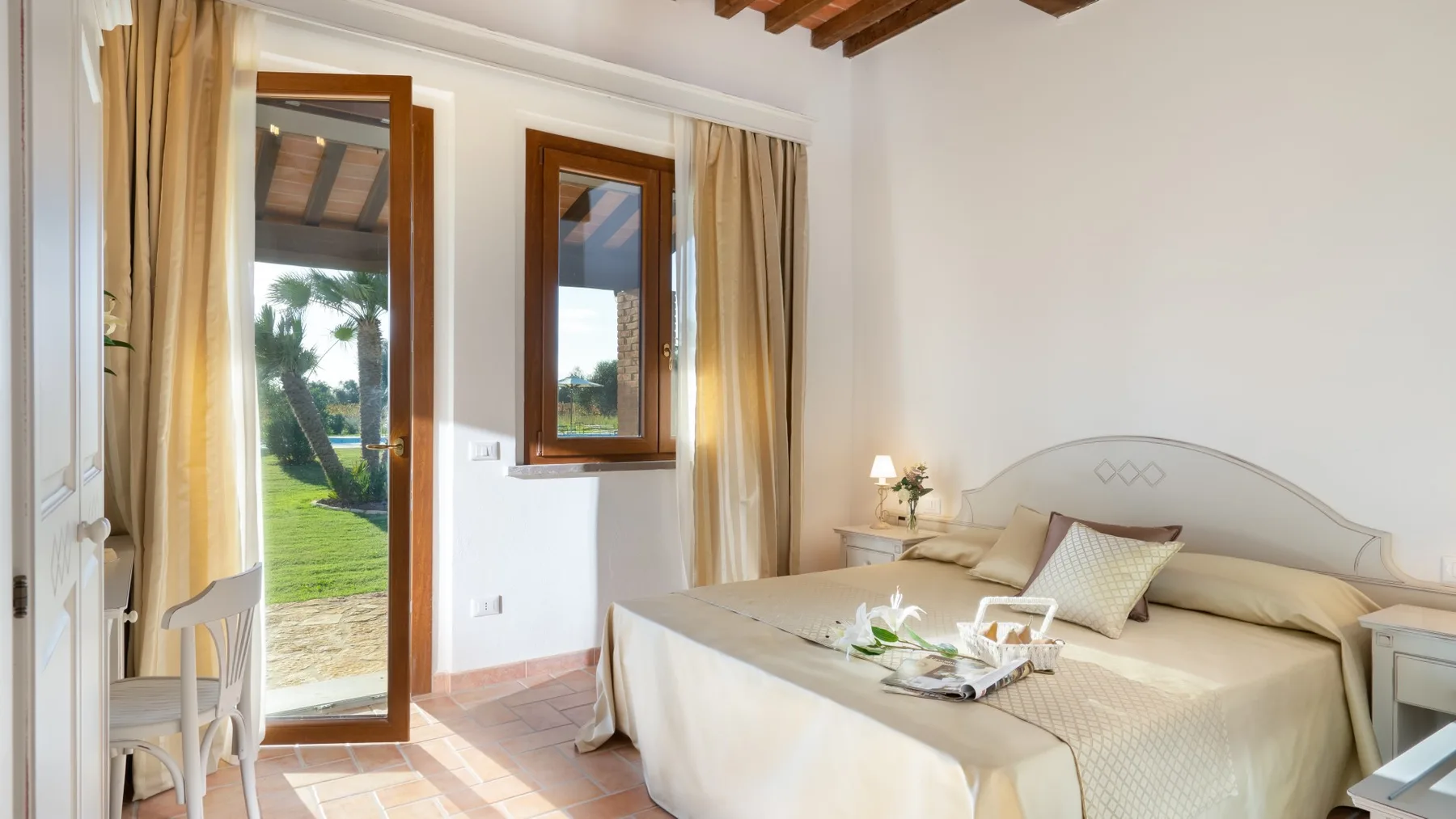 A bright bedroom with a large bed beside windows overlooking a garden.