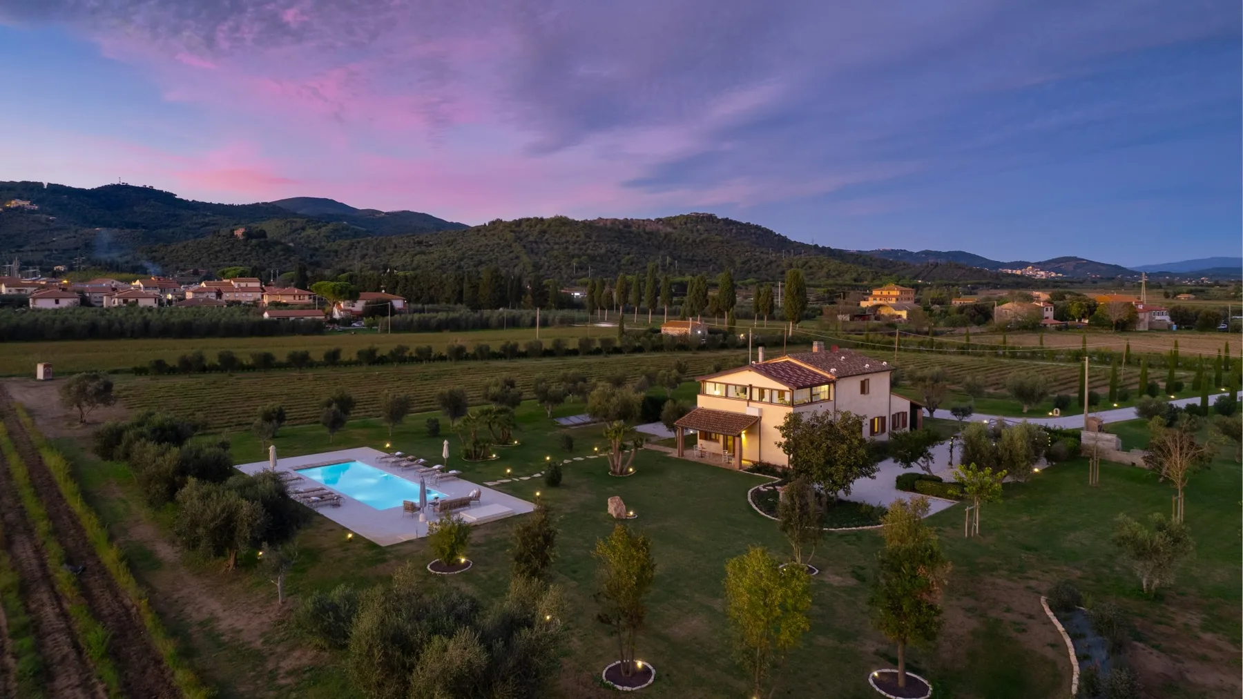 A countryside property with a house, swimming pool, and surrounding hills at dusk.