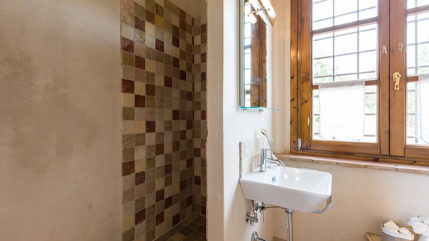 A bathroom with a wall-mounted sink beside a tiled shower area.
