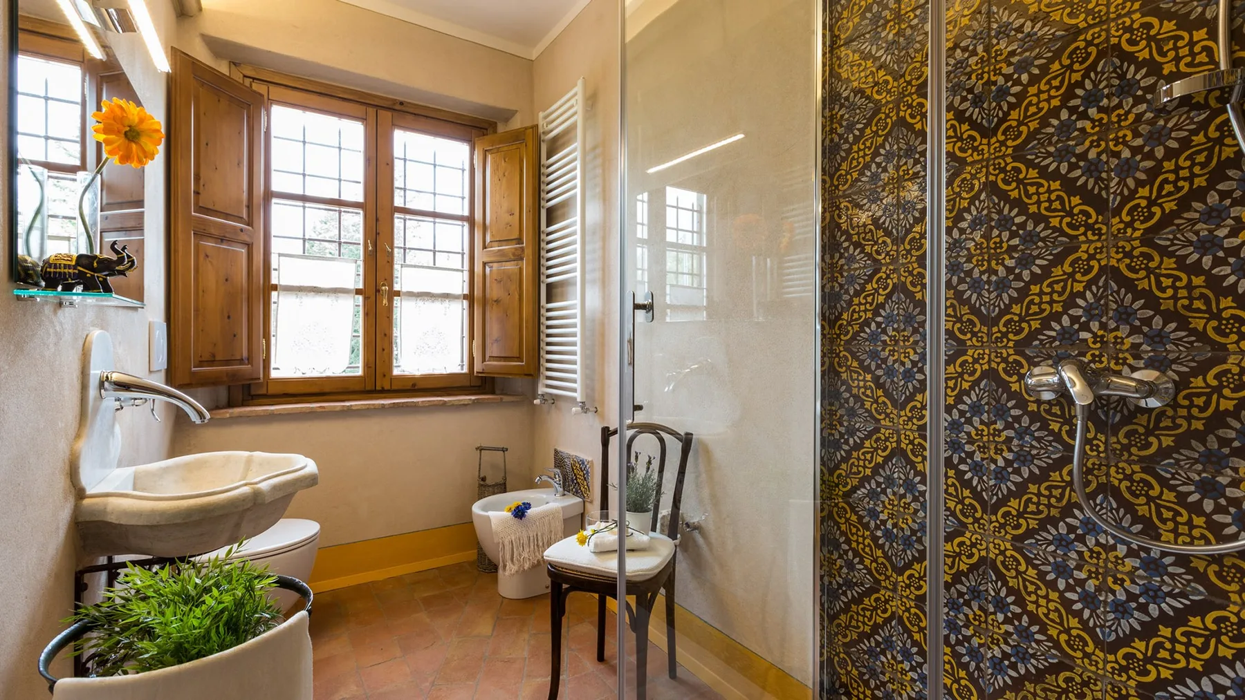 A bathroom with a sink, a window, and a patterned shower area.