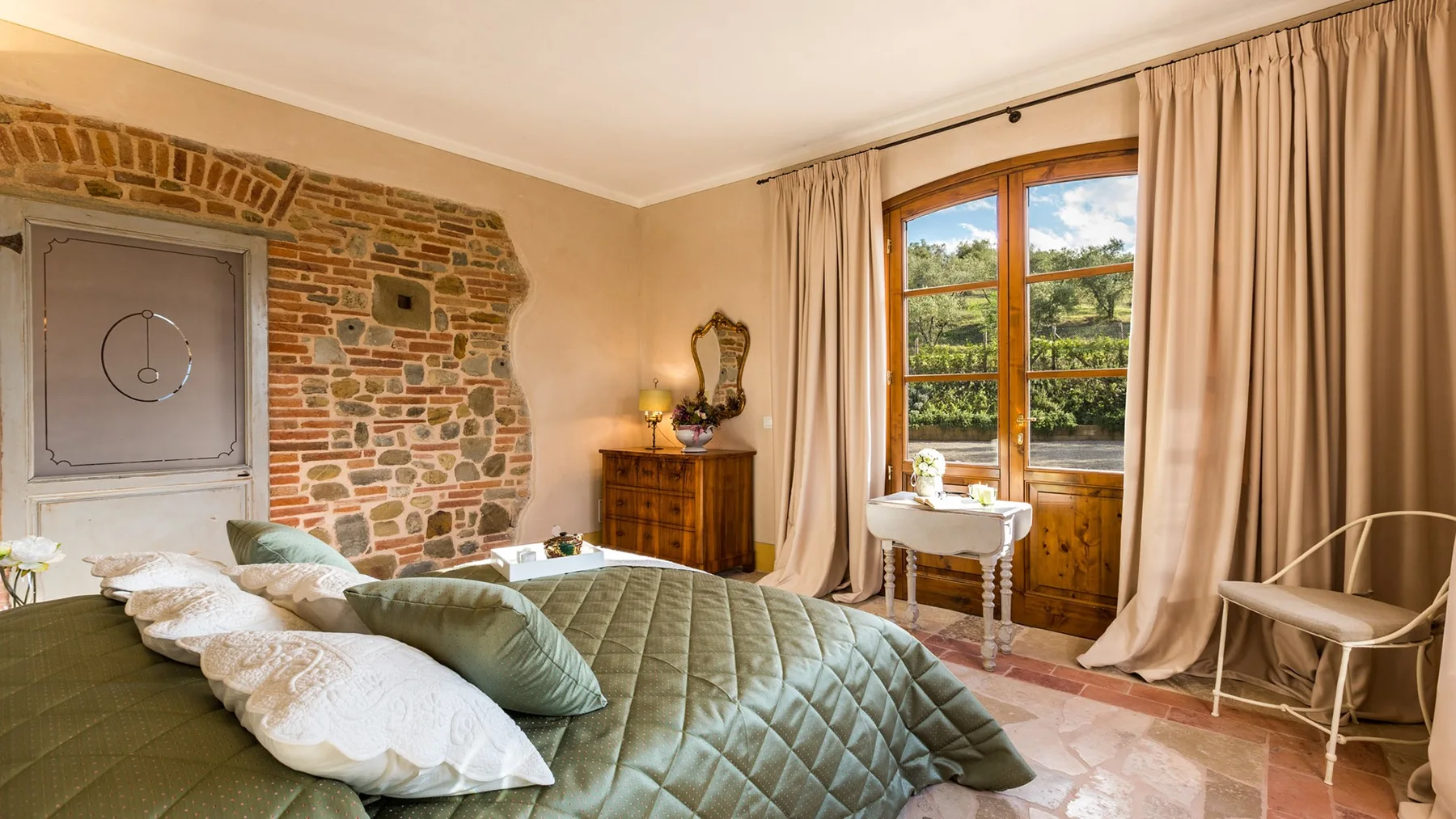 A bedroom with a large bed beside a window overlooking greenery.
