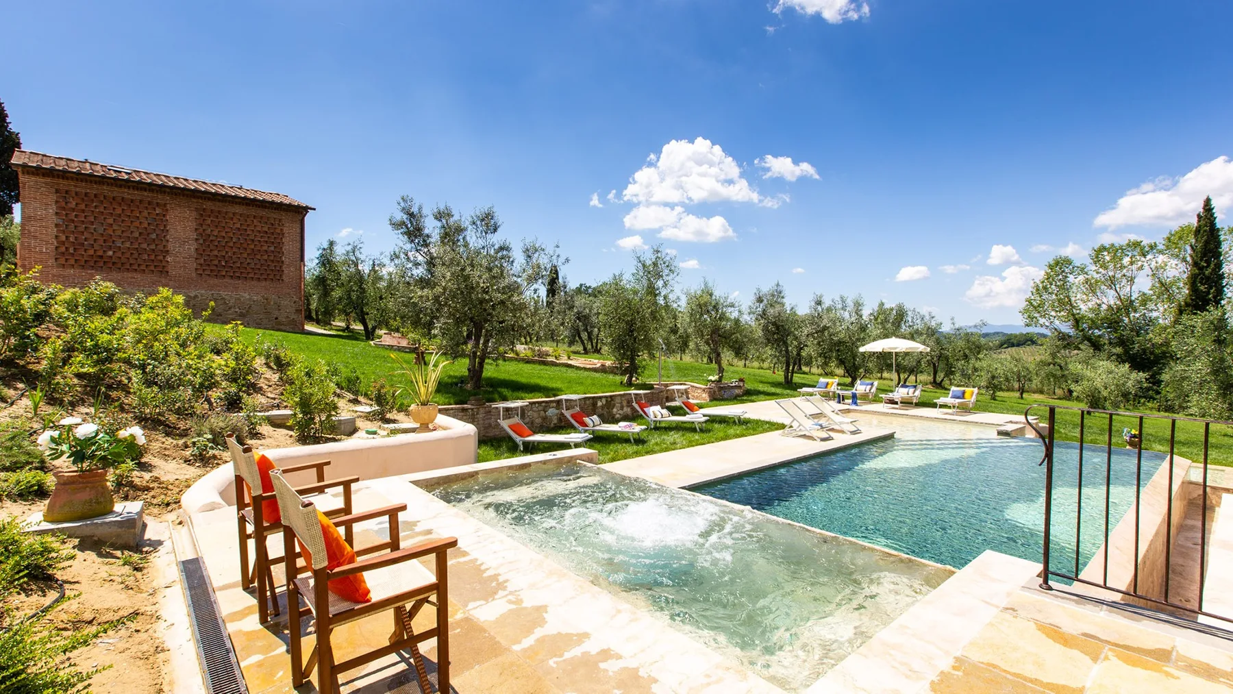 An outdoor pool area with bubbling water, seating, and a sunny garden.