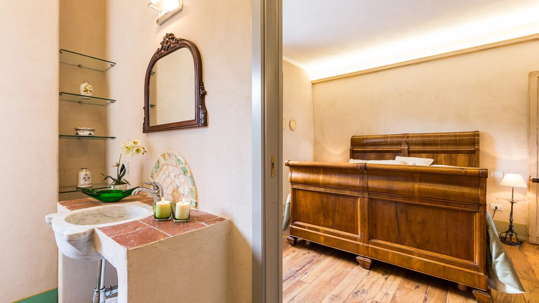 A bathroom vanity opens onto a bedroom with a large wooden bed.
