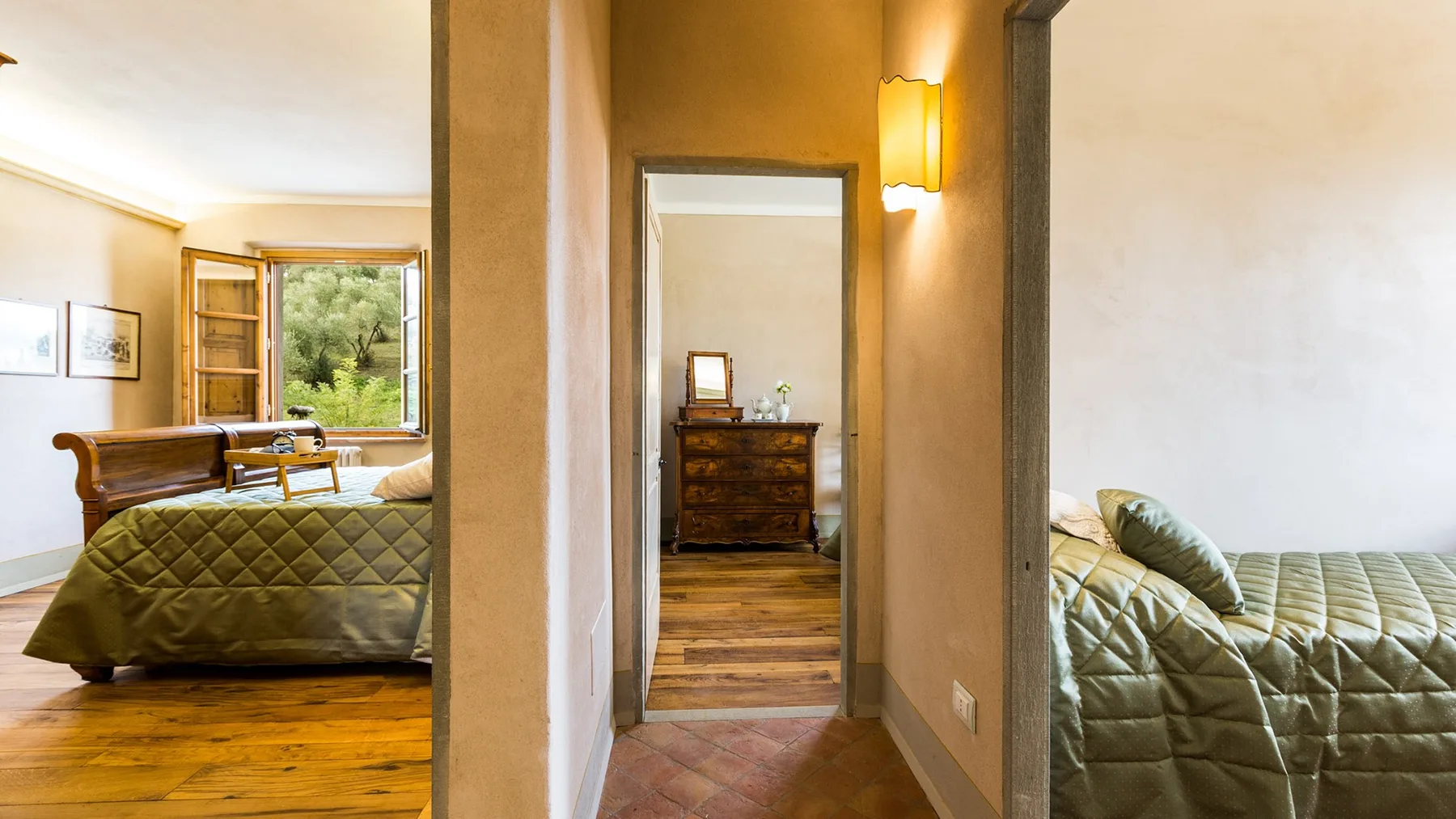 A bedroom with a quilted bed beside an open doorway to another room.