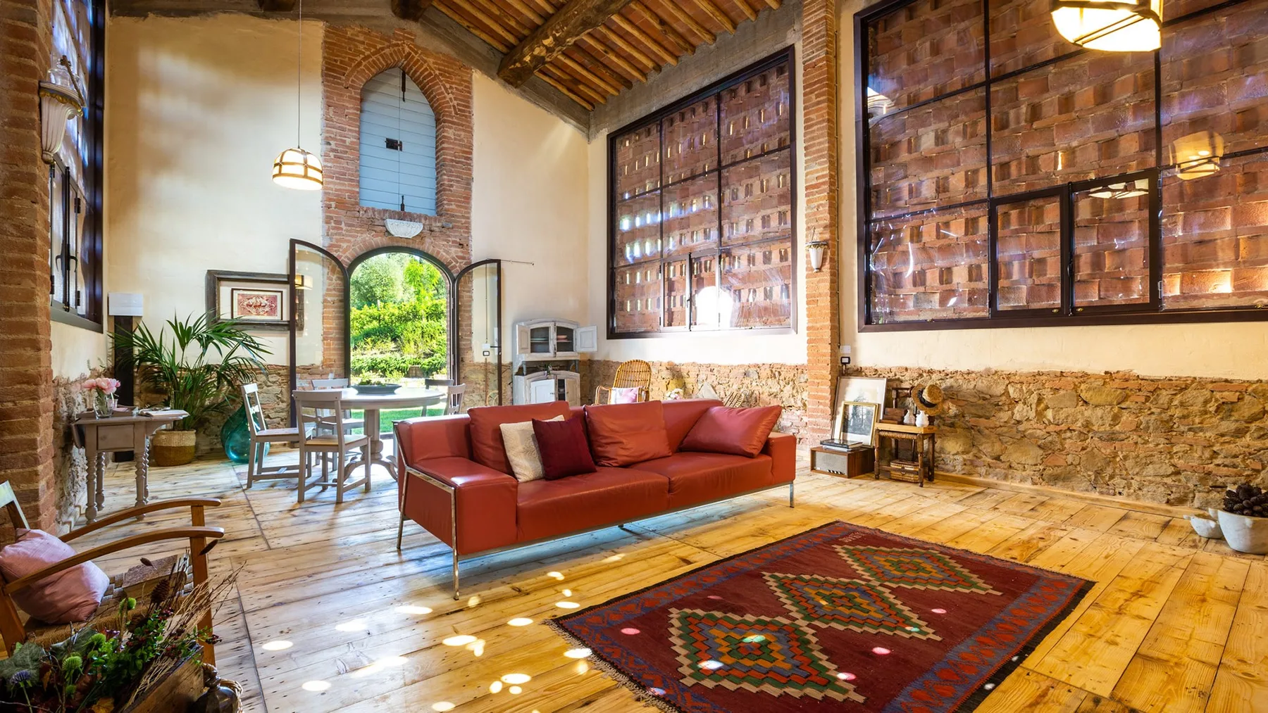 A rustic living room with red seating and large brick-framed windows.