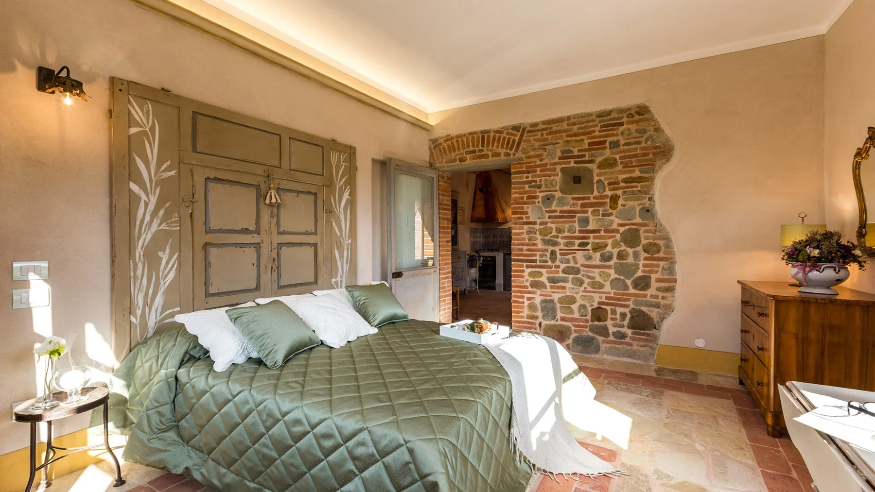 A bedroom with a neatly made bed and a stone accent wall.