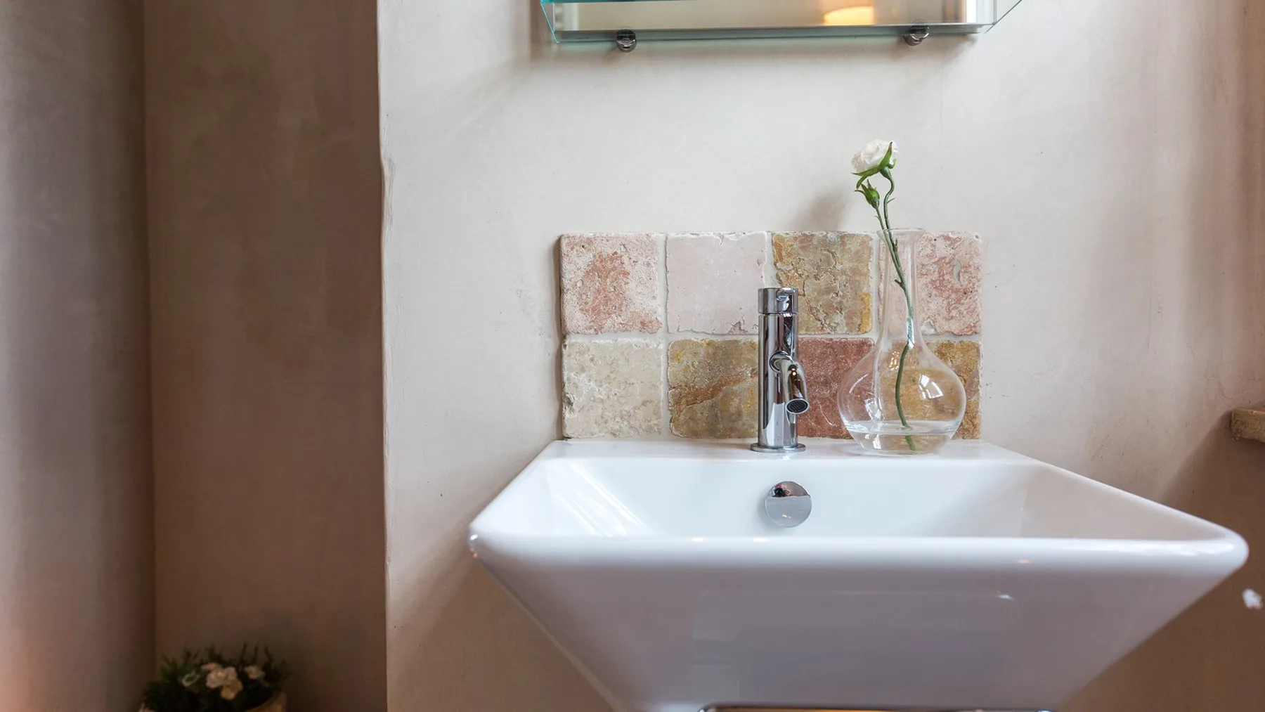 A bathroom sink sits beneath a mirror, with a small vase beside the faucet.